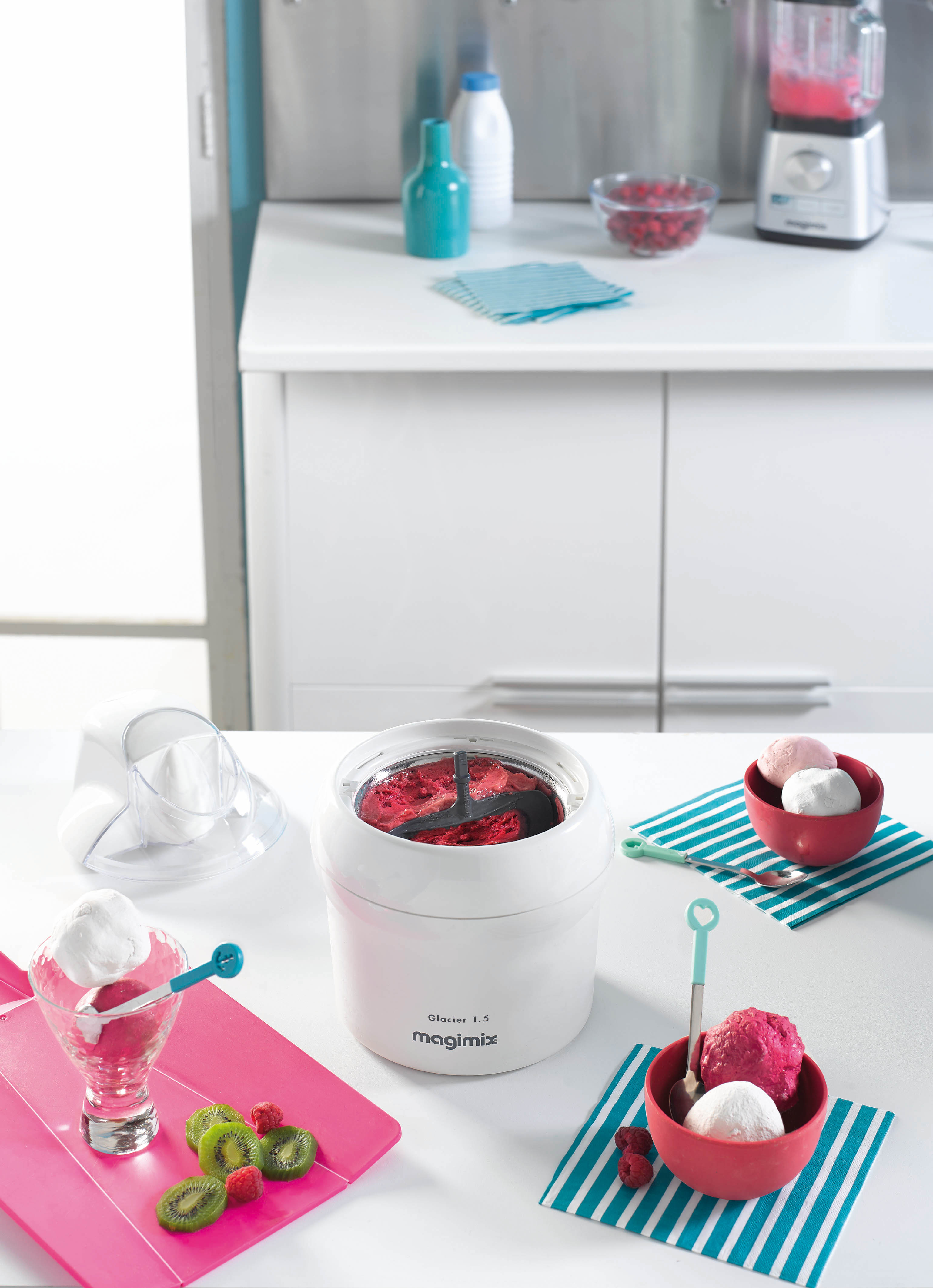 An ice cream maker with red ice cream. Various bowls and accessories are around.