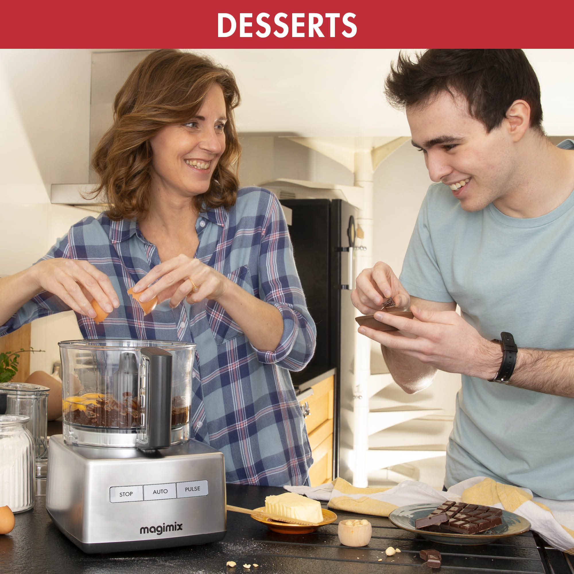 Two people preparing a dessert with a food processor. Ingredients like eggs, chocolate, and butter are present.