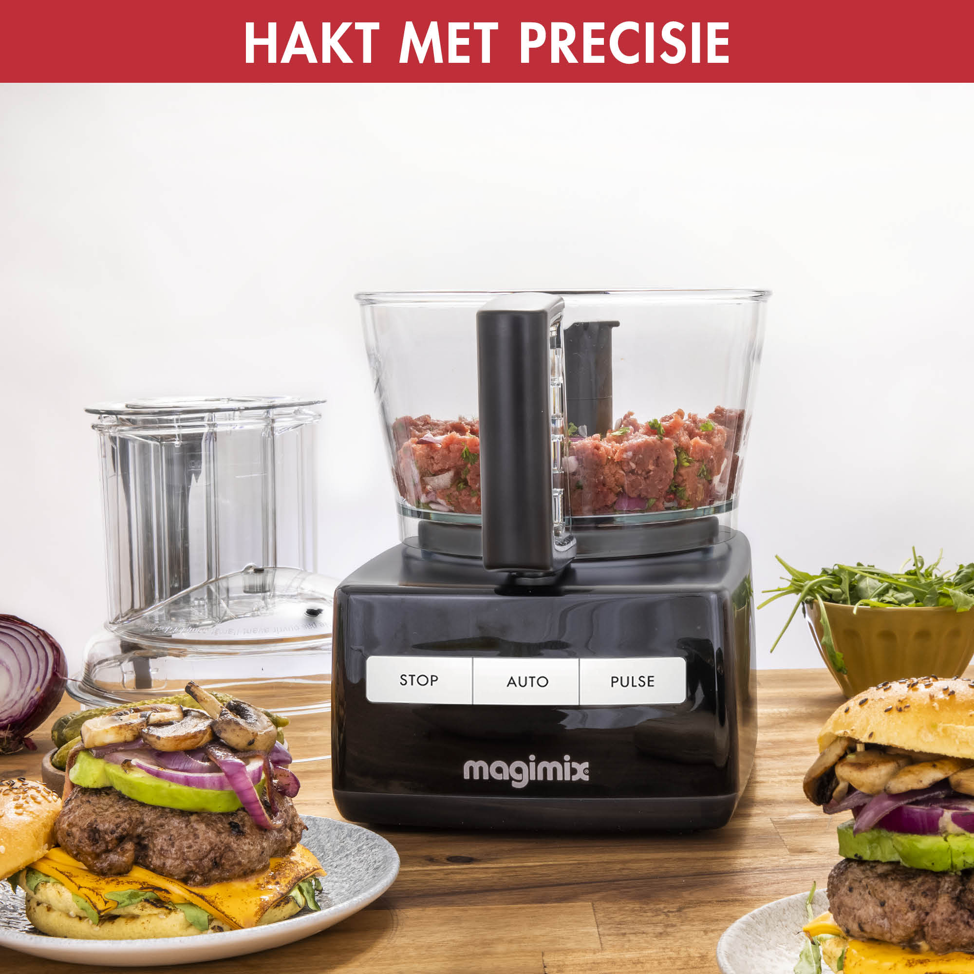 A food processor with burgers, onion and greens. Two burgers are ready to serve and one is being made.