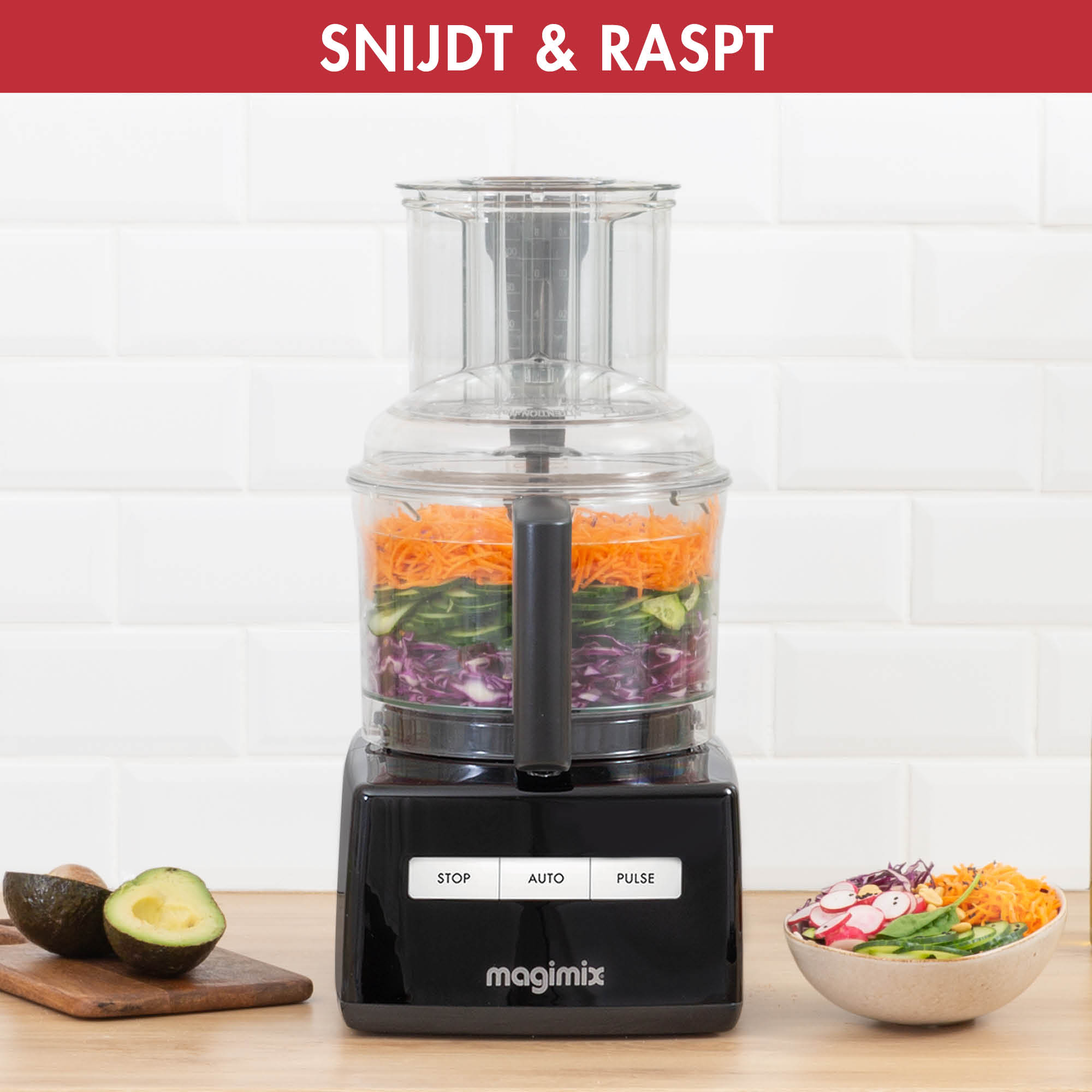 A black food processor with ingredients inside. Sliced vegetables and a bowl of salad are also on the scene.