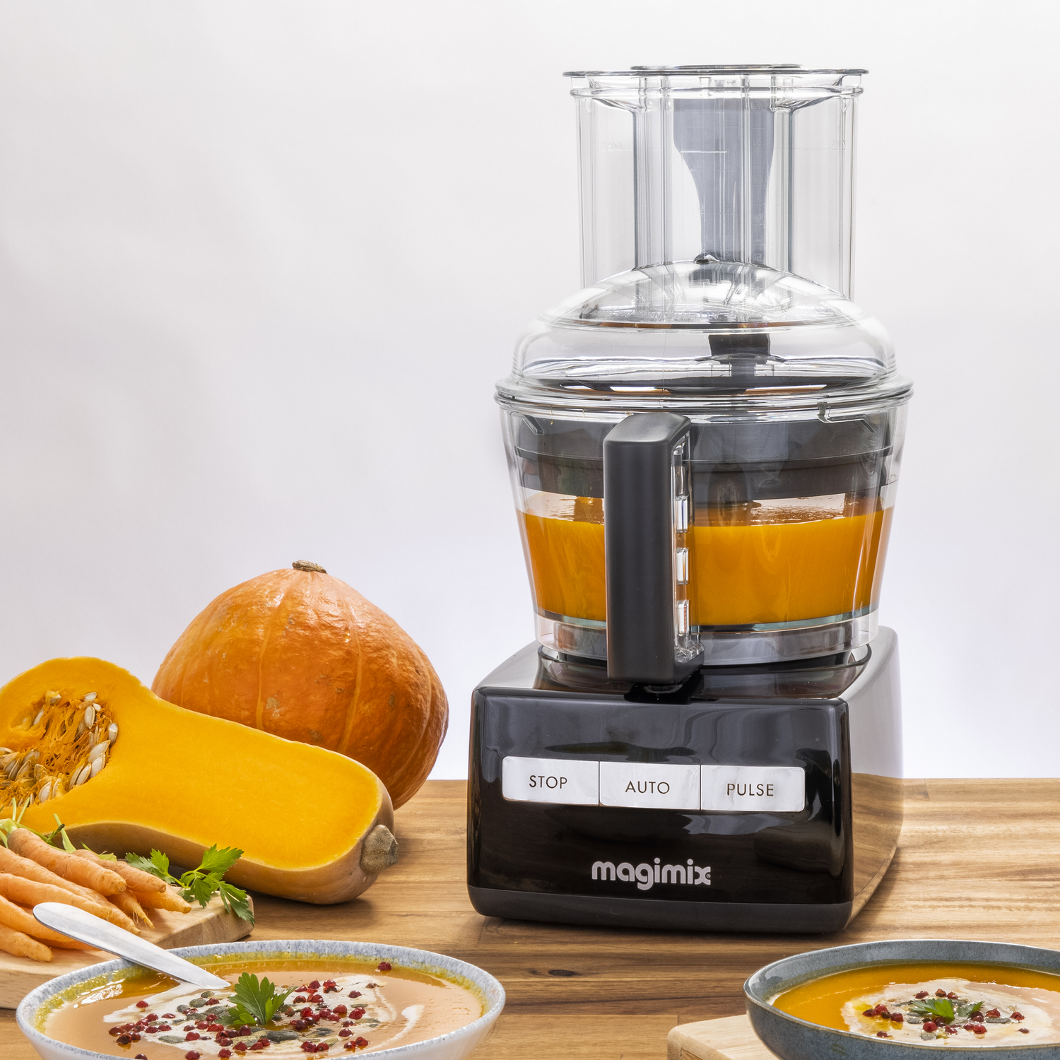 Keukenmachine met pompoenen, wortels en soep, samen met kommen en ingrediënten.