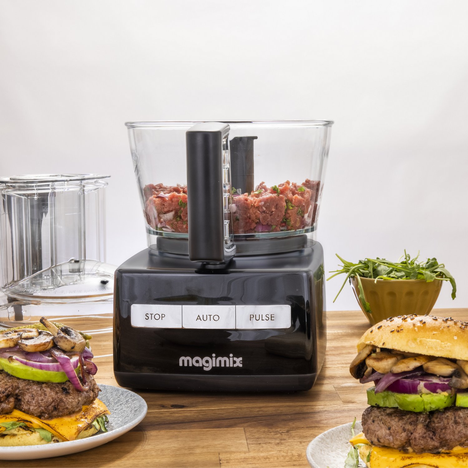 Keukenmachine met burgeringrediënten en twee burgers op borden.