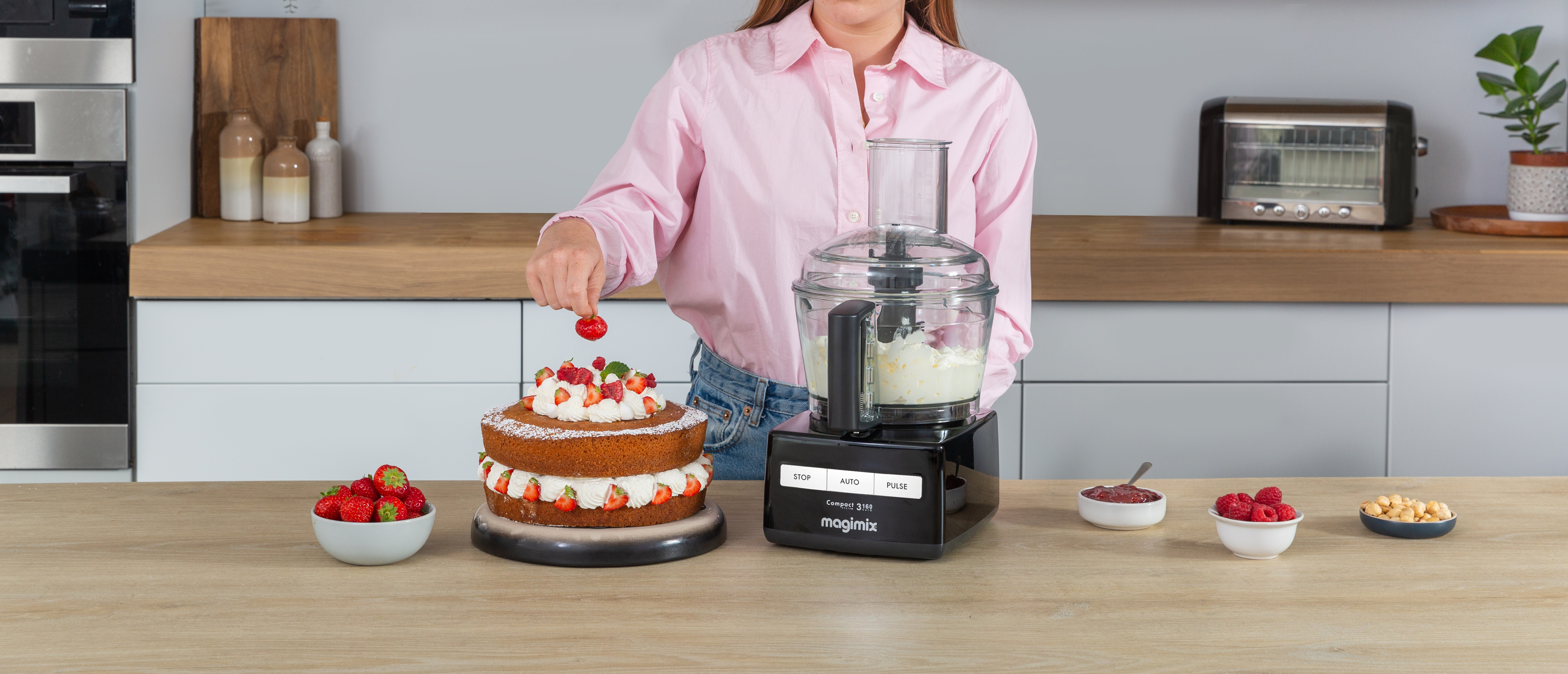 Vrouw die een cake maakt met een keukenmachine. Cake en ingrediënten op het aanrecht.