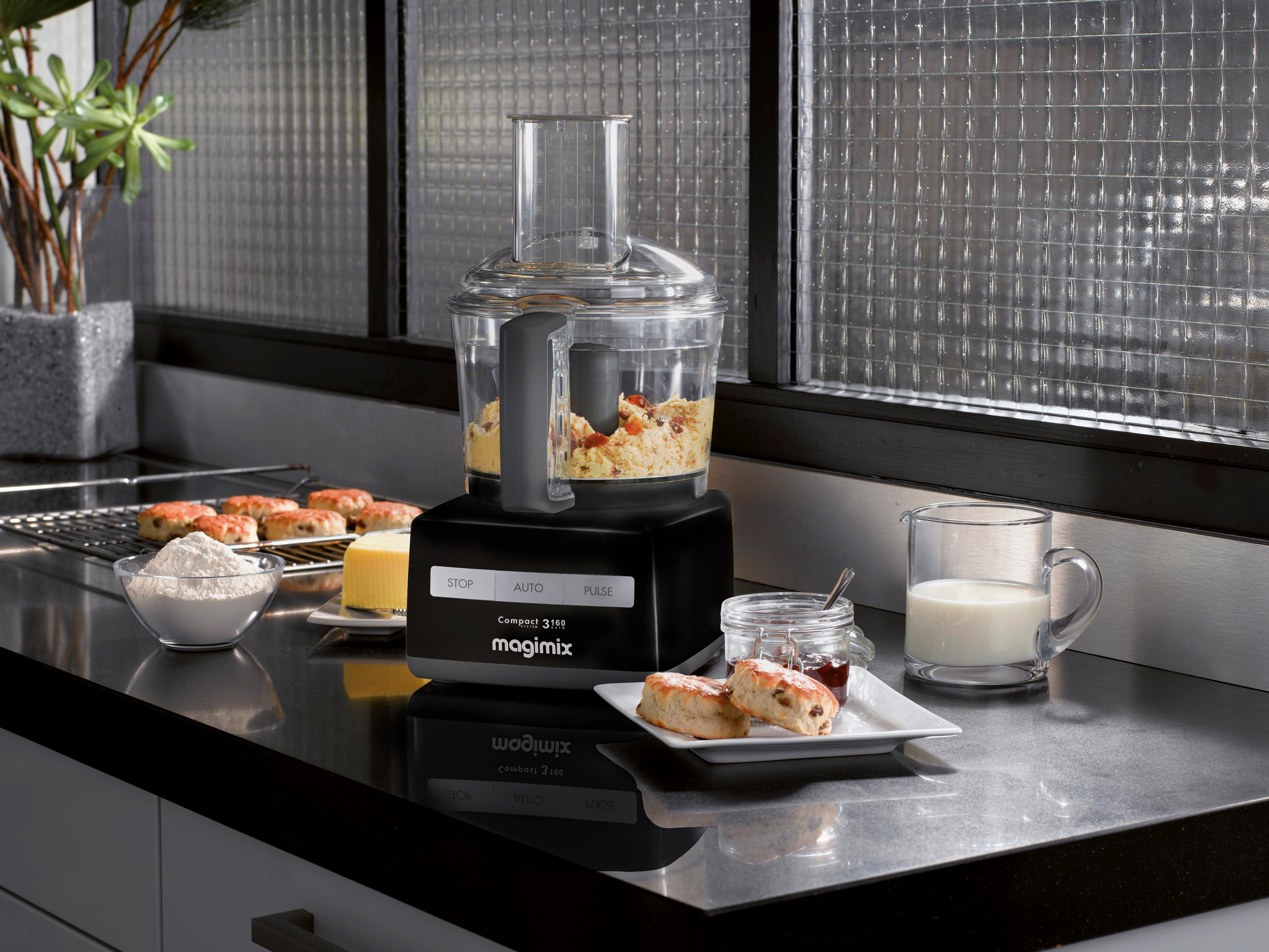 Keukenmachine met eten, plus bakwaren, melk en jam op een aanrecht.