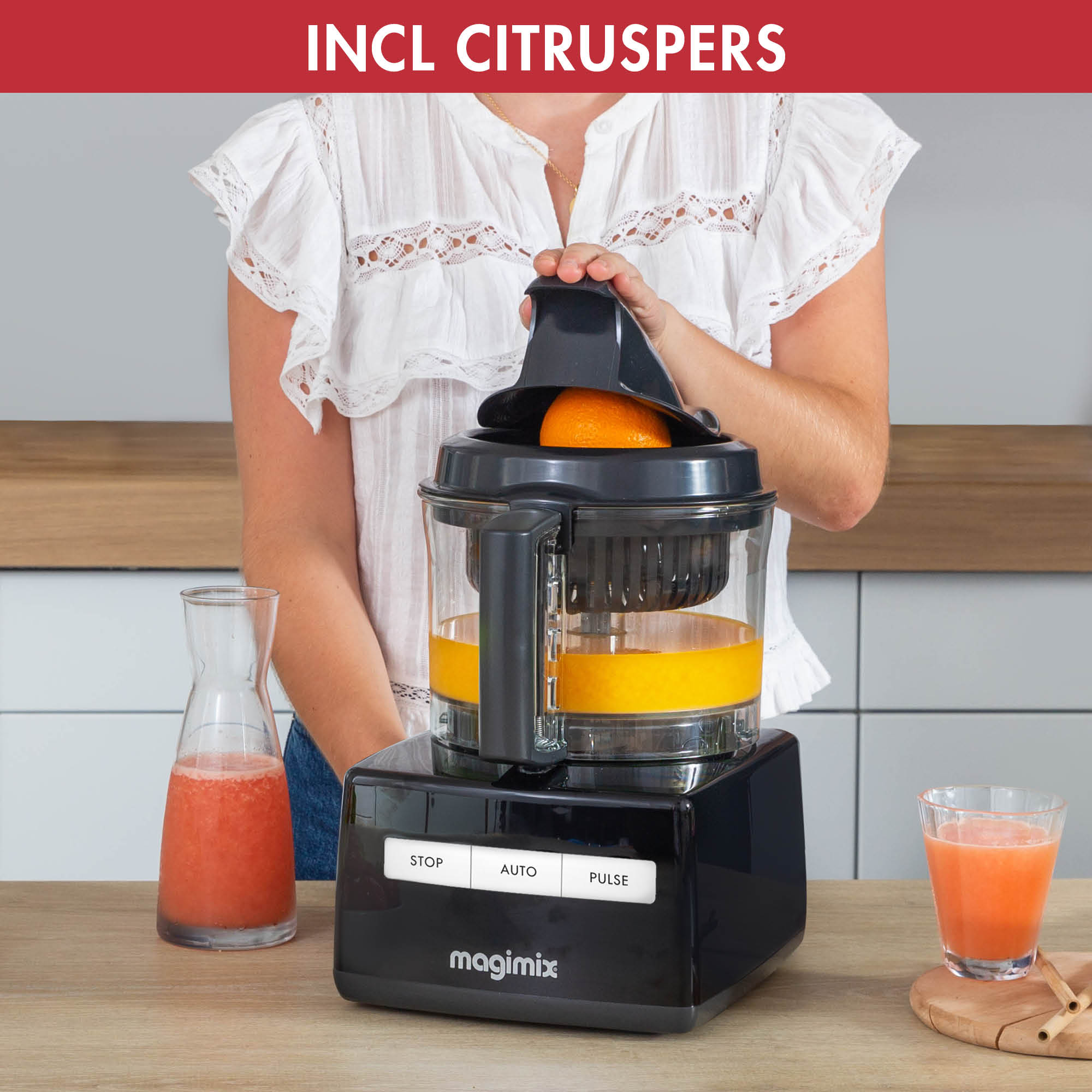 Woman using a food processor with an orange. Juice is collecting. Decanter and glass of juice nearby.