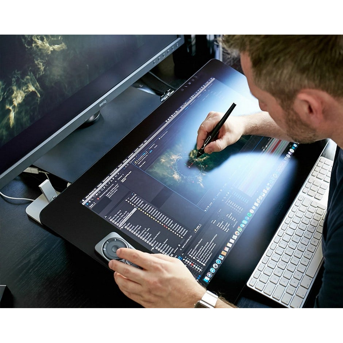 Mężczyzna pracuje na tablecie graficznym za pomocą pióra. Na biurku znajduje się monitor i klawiatura.