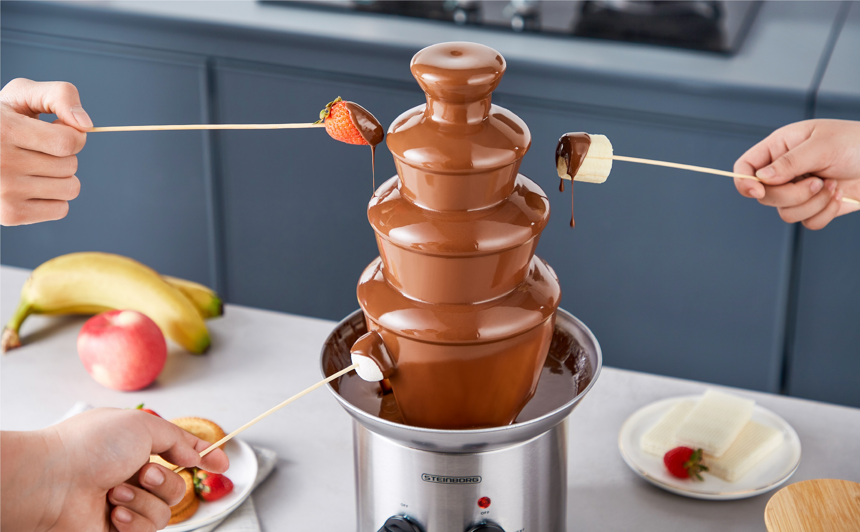 Schokoladenbrunnen mit Fruchtspießen. Leute tauchen Früchte in Schokolade. Marshmallows, Bananen, Erdbeeren.
