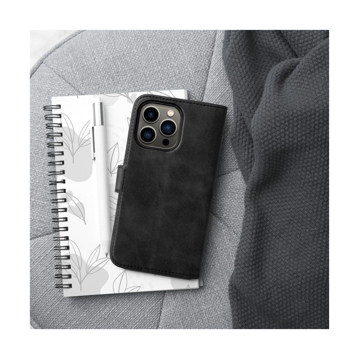 Custodia nera per telefono su quaderno, penna e coperta grigia.