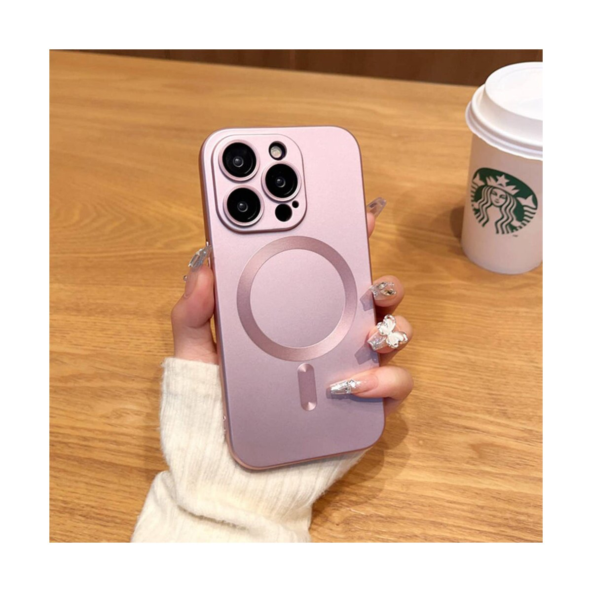 La mano di una persona tiene una custodia rosa con un cerchio MagSafe, una tazza di caffè a destra.