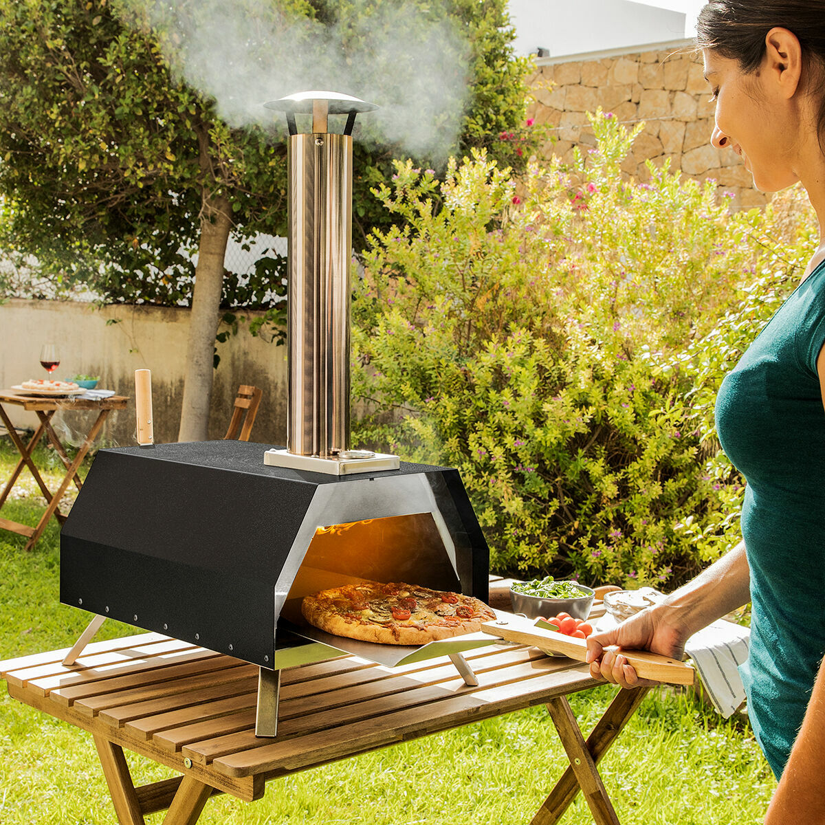 Una persona usa un forno per pizza all'aperto su un tavolo di legno in giardino.