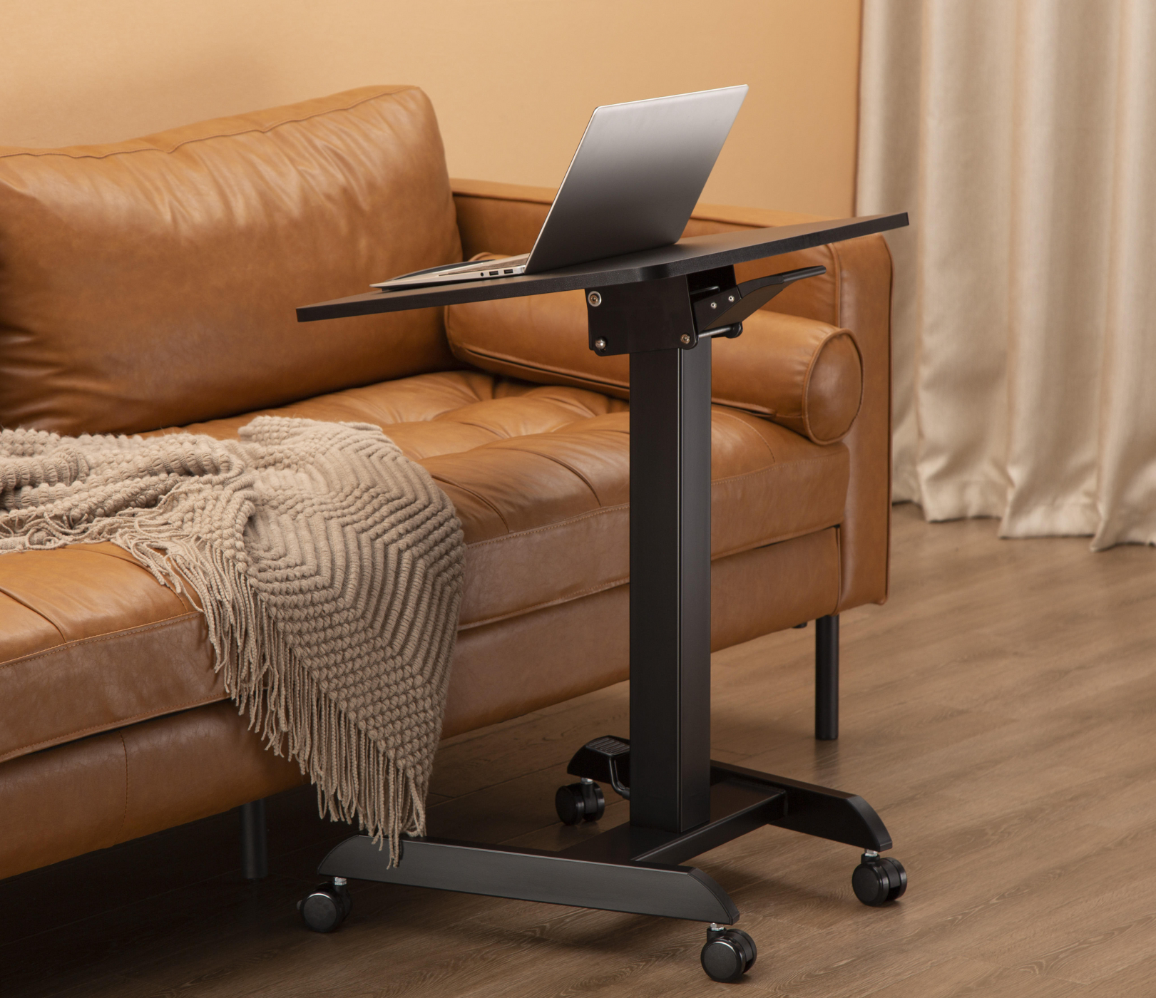Een zwarte laptoptafel met wielen, een laptop staat op de tafel.