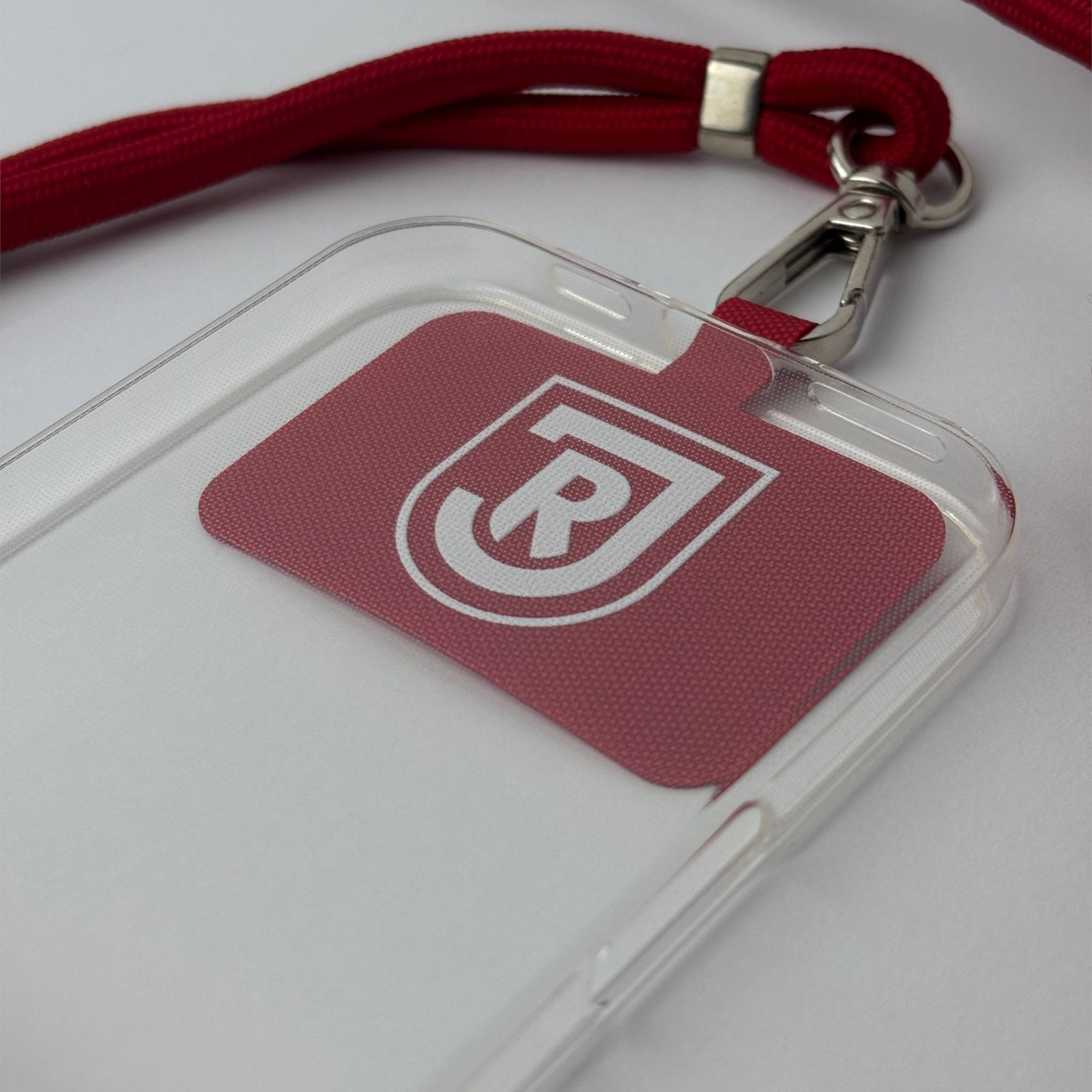 Transparente Handyhülle mit rotem Umhängeband und rotem Logo mit weißen Buchstaben, Nahaufnahme.