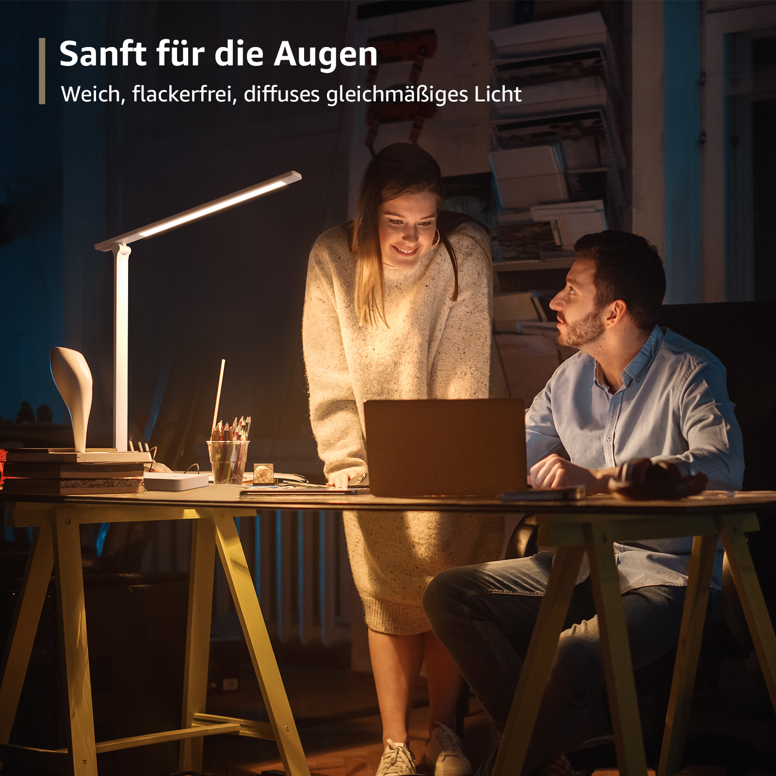 Ein Mann und eine Frau schauen auf einen Laptop auf einem Schreibtisch, der von einer Schreibtischlampe beleuchtet wird.