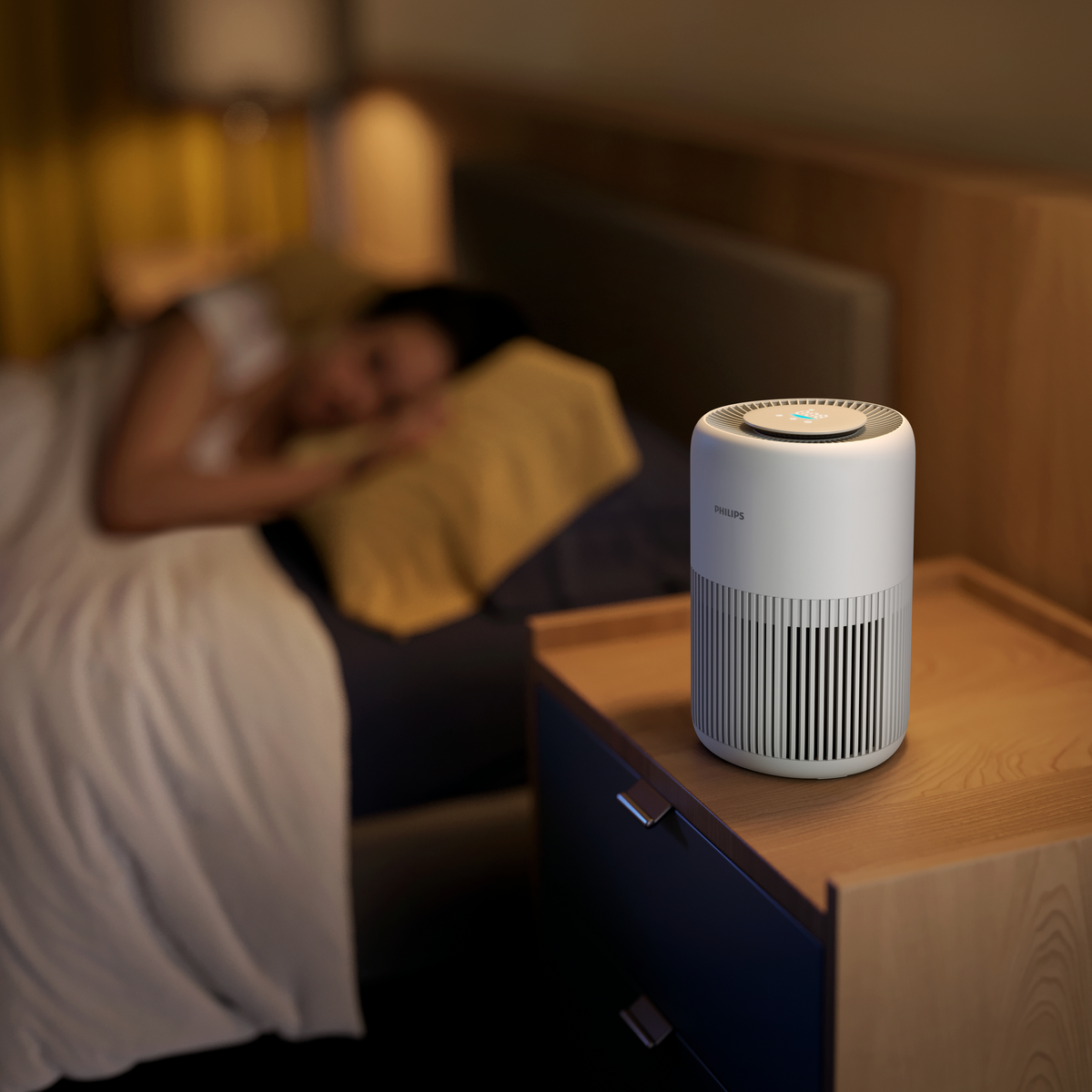 Persona durmiendo en la cama con purificador de aire en una mesita de noche. Pared amarilla.