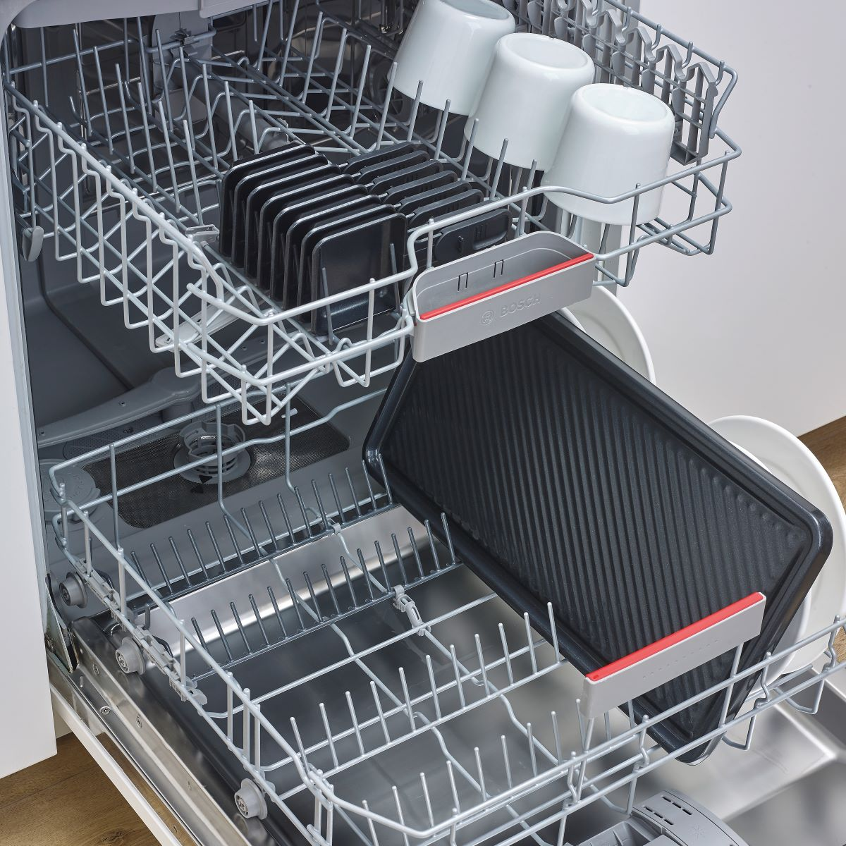 Wnętrze zmywarki z koszami, naczyniami i tacami, z logo Bosch z przodu.