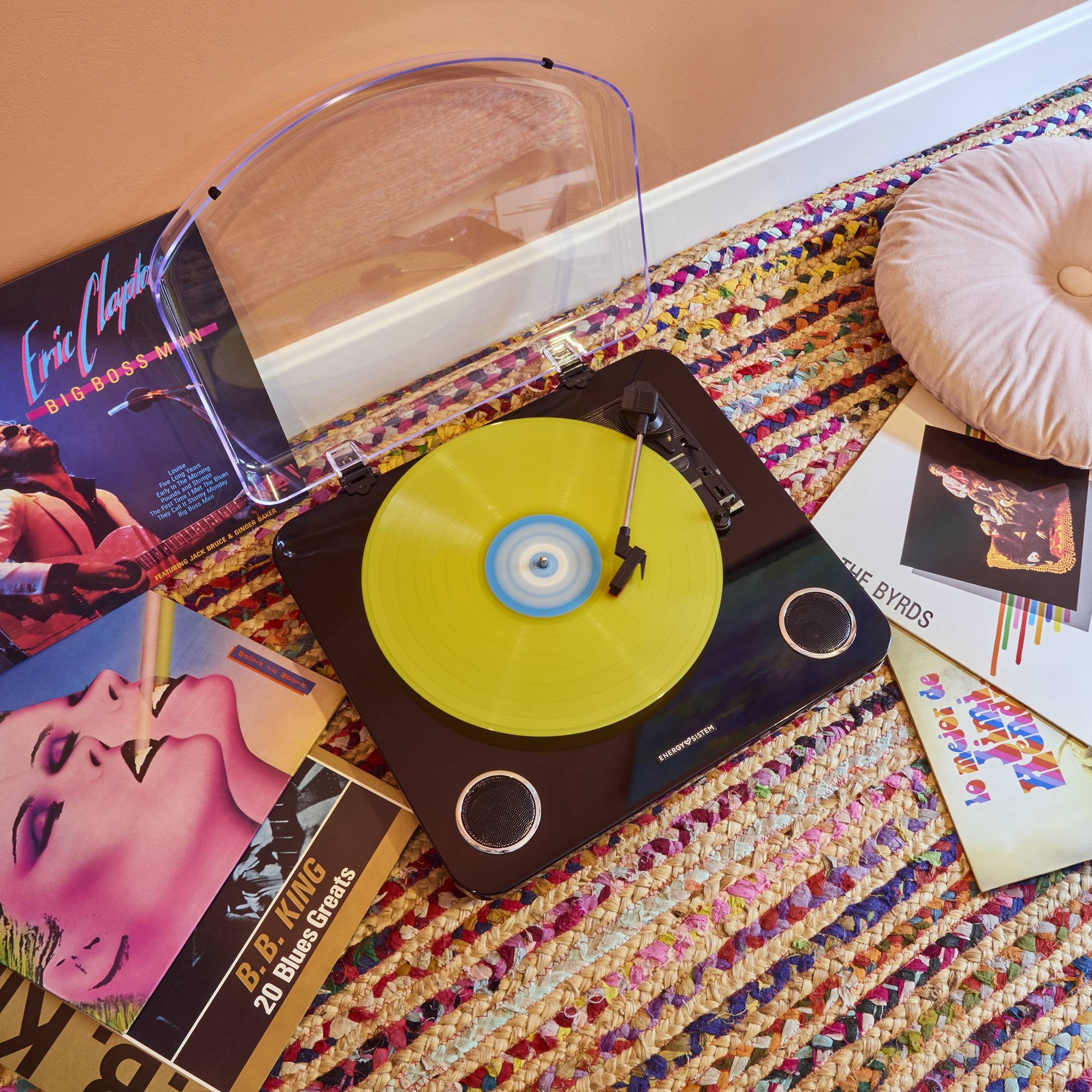 Tocadiscos con un disco amarillo sobre una alfombra tejida colorida y portadas musicales.