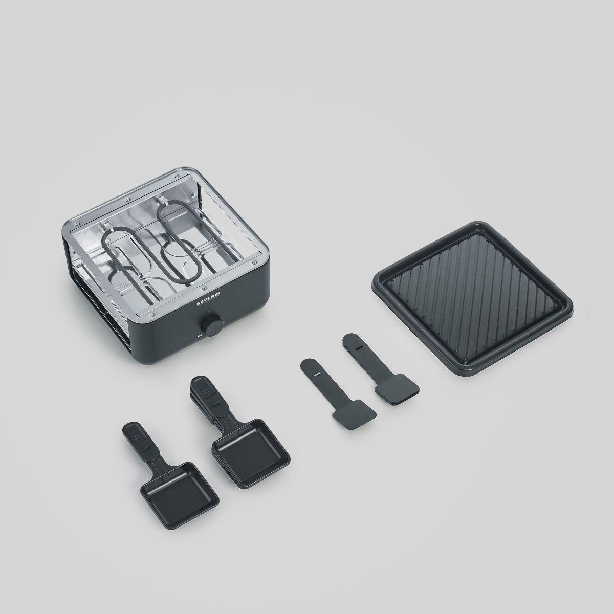 Mały grill elektryczny i akcesoria. Trzy mini patelnie, płyta grillowa. Białe tło.