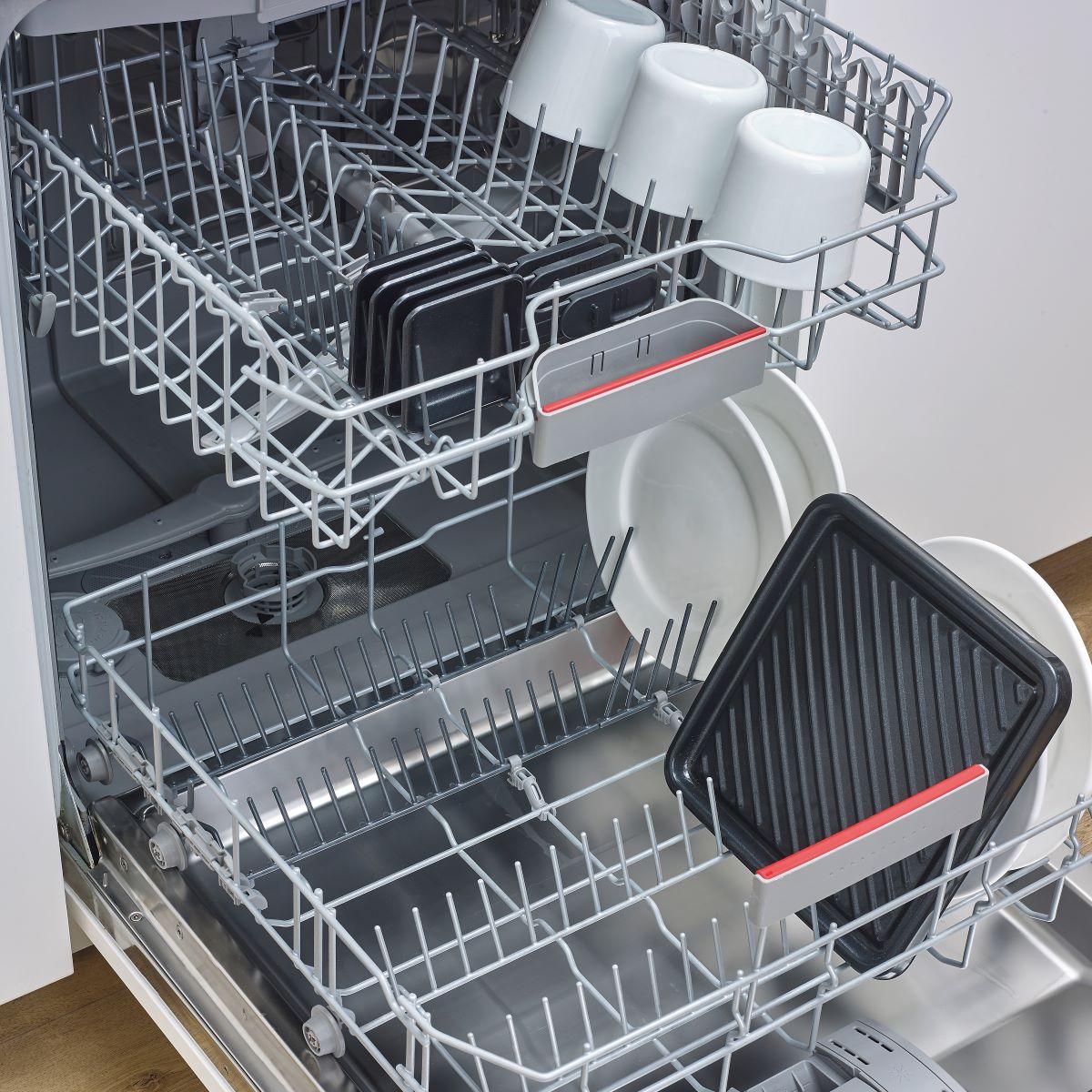 Wnętrze zmywarki z naczyniami, kubkami i patelnią grillową. Otwarte drzwi, wnętrze ze stali nierdzewnej.