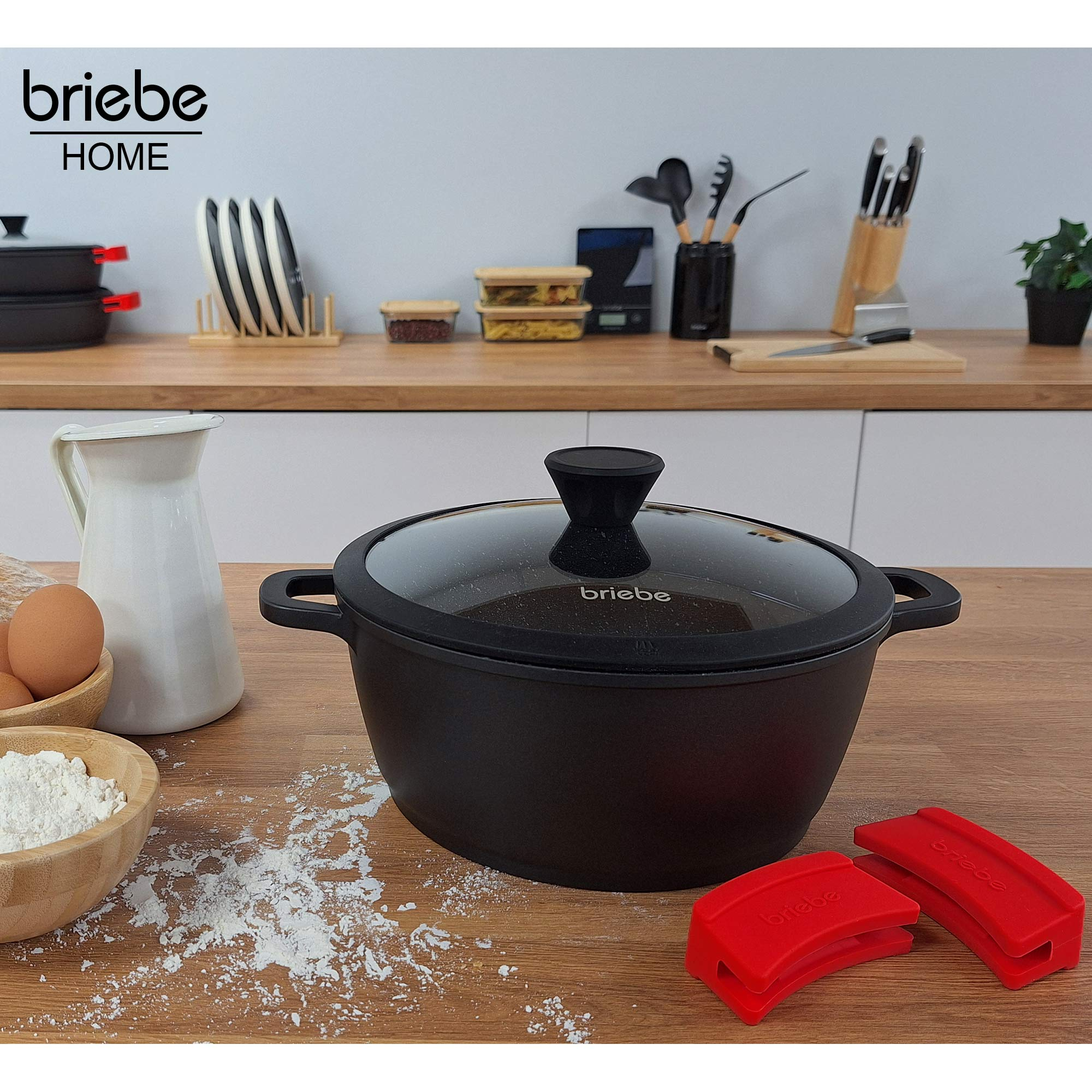 Olla negra sobre una mesa de madera con otros utensilios de cocina, fondo blanco.