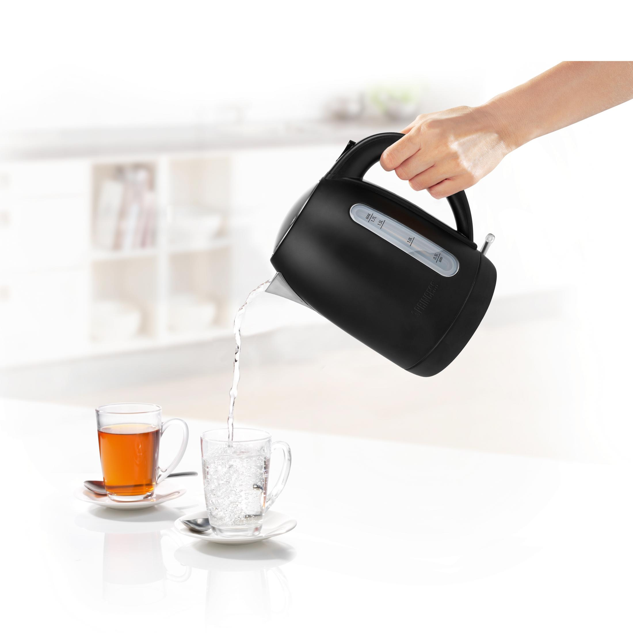 Czarny czajnik wlewa wodę do szklanki. Dwie szklanki i spodki na białej powierzchni.