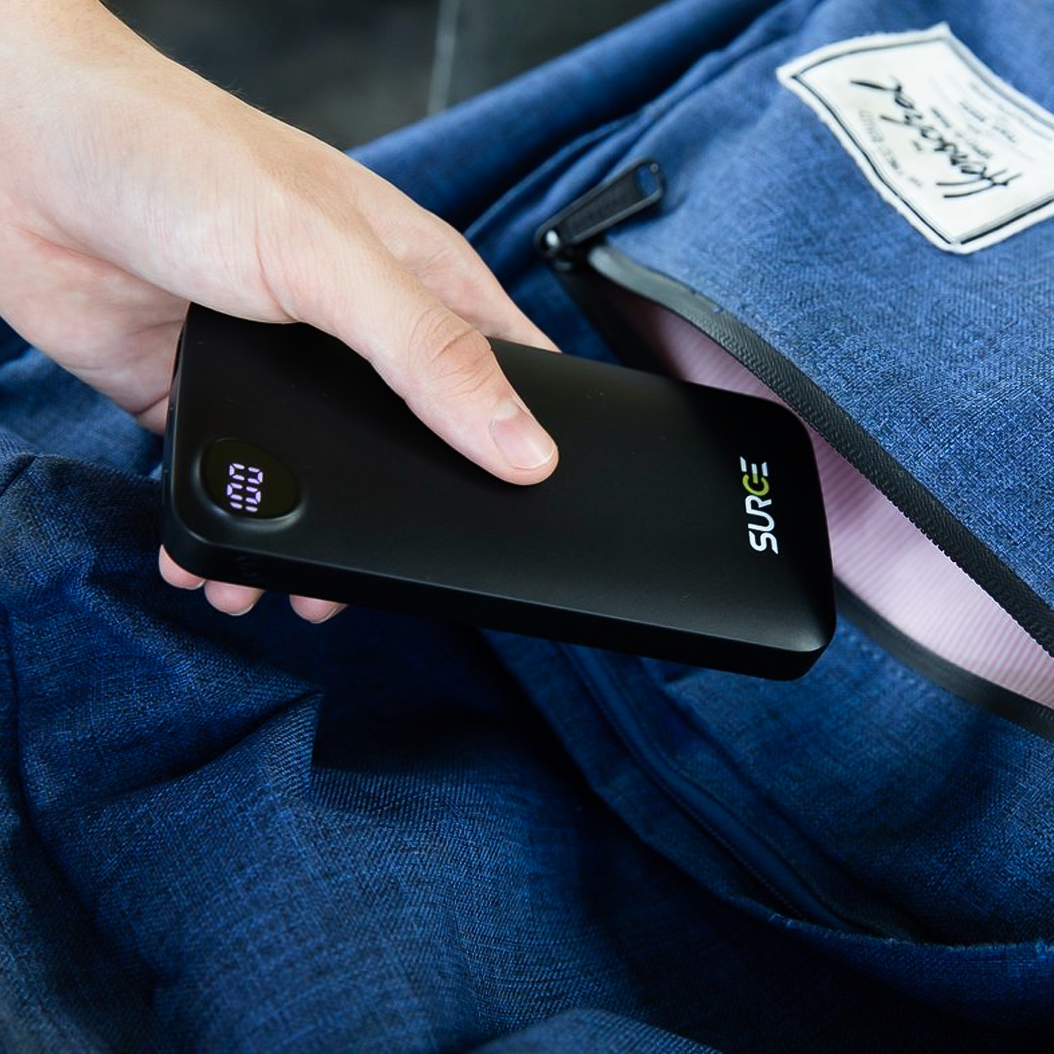 Hand inserting a black power bank into a blue backpack pocket.