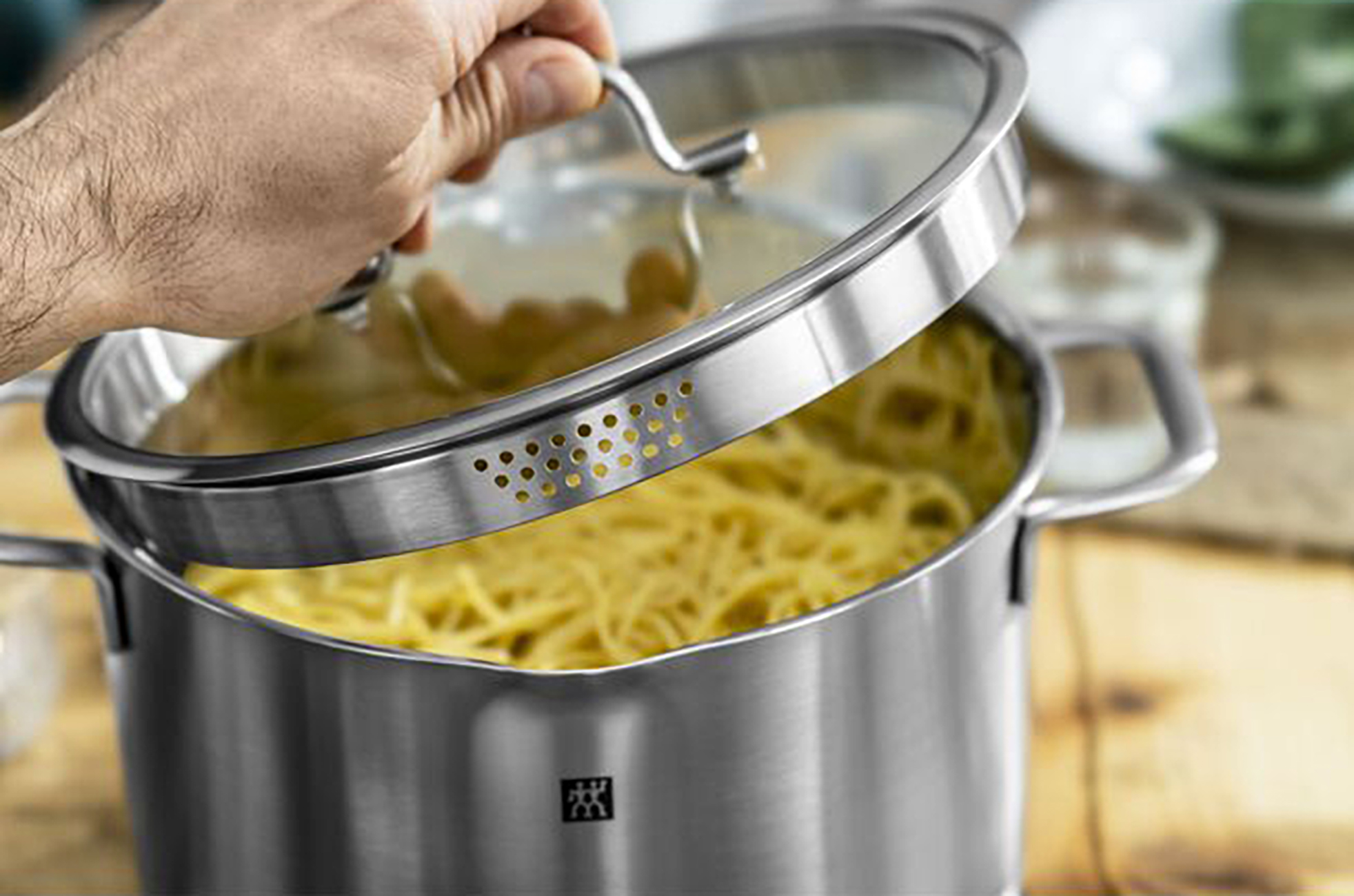 Osoba otwierająca garnek ze stali nierdzewnej z makaronem w środku.