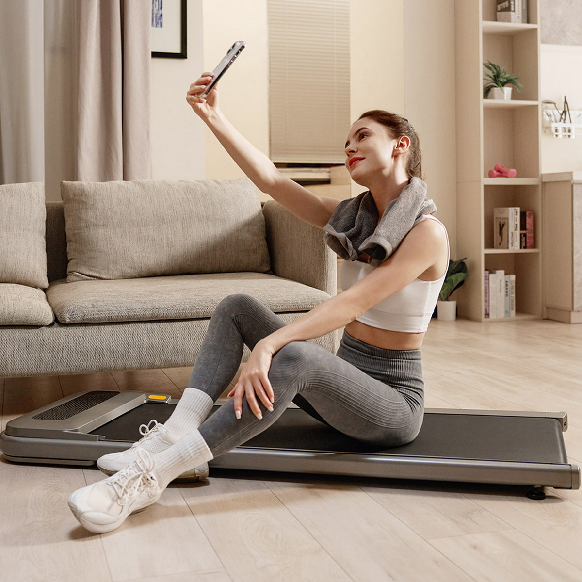 Frau macht Selfie auf Laufband. Sofa und Regale im Hintergrund.