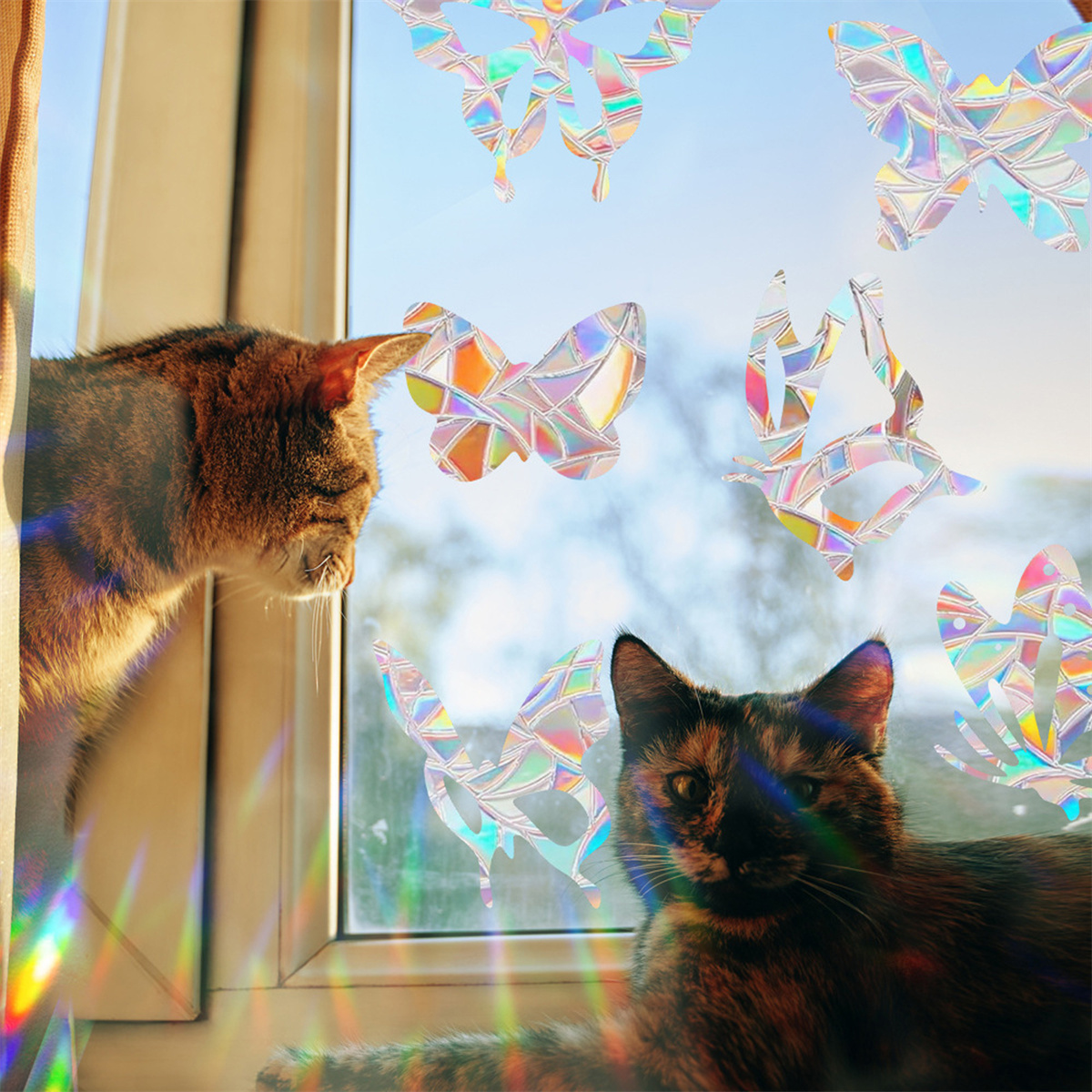 Zwei Katzen betrachten bunte Schmetterlingsaufkleber an einem Fenster.