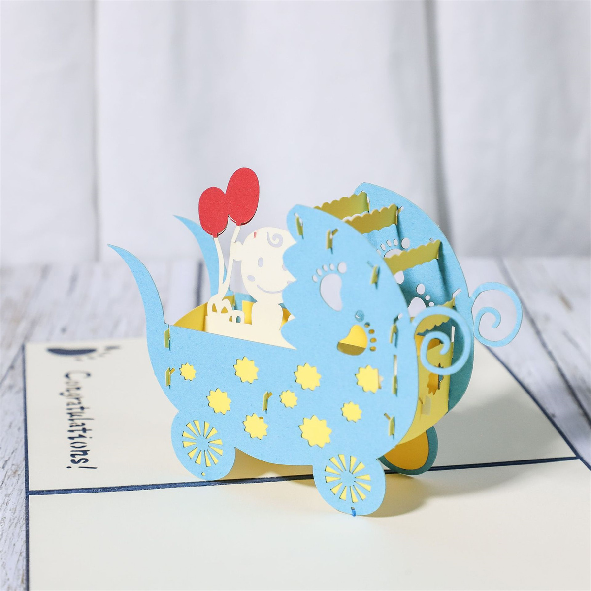 Eine Pop-up-Babywagenkarte. Blaue und gelbe Farben. Luftballons und ein Babyausschnitt innen.