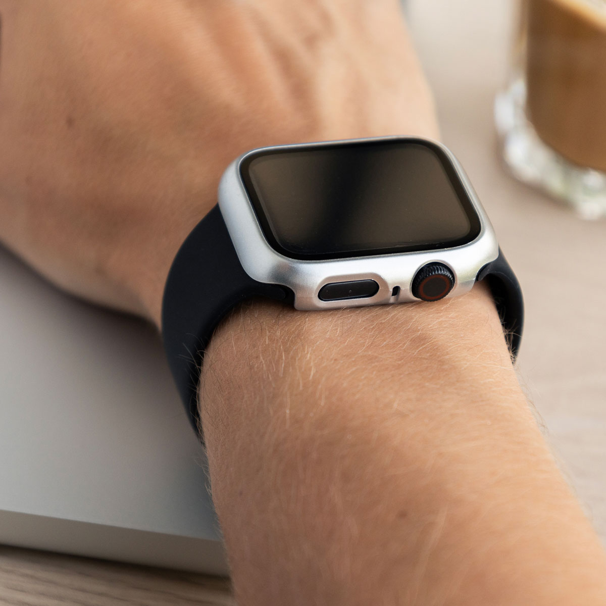 Wrist with a black watch, silver case. Coffee cup in the background.
