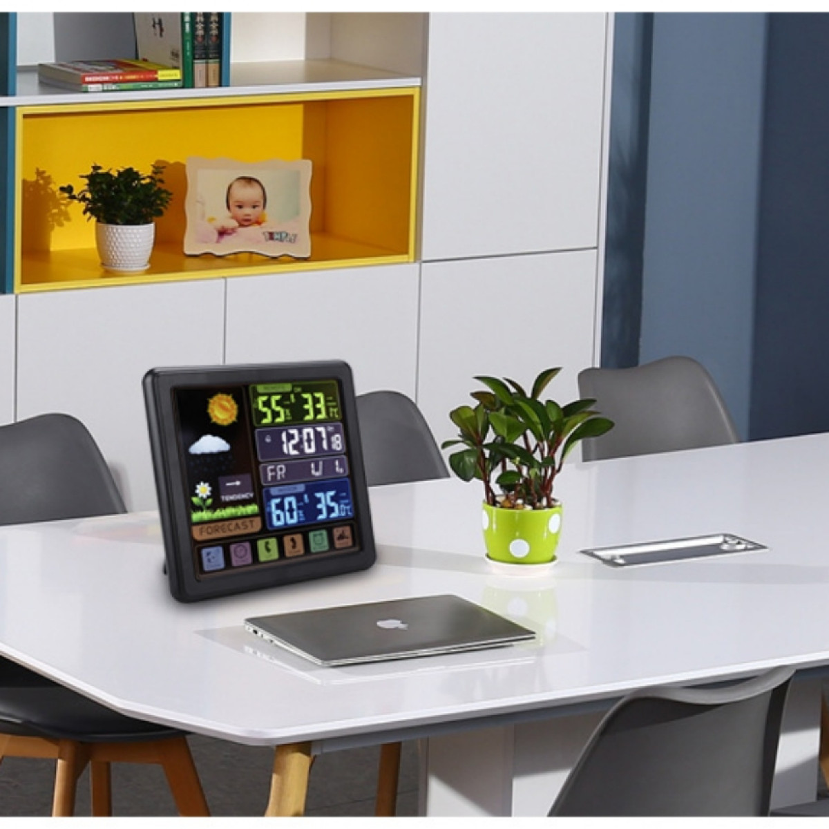 Cyfrowa stacja pogodowa na białym stole z laptopem i małą rośliną w zielonej doniczce.