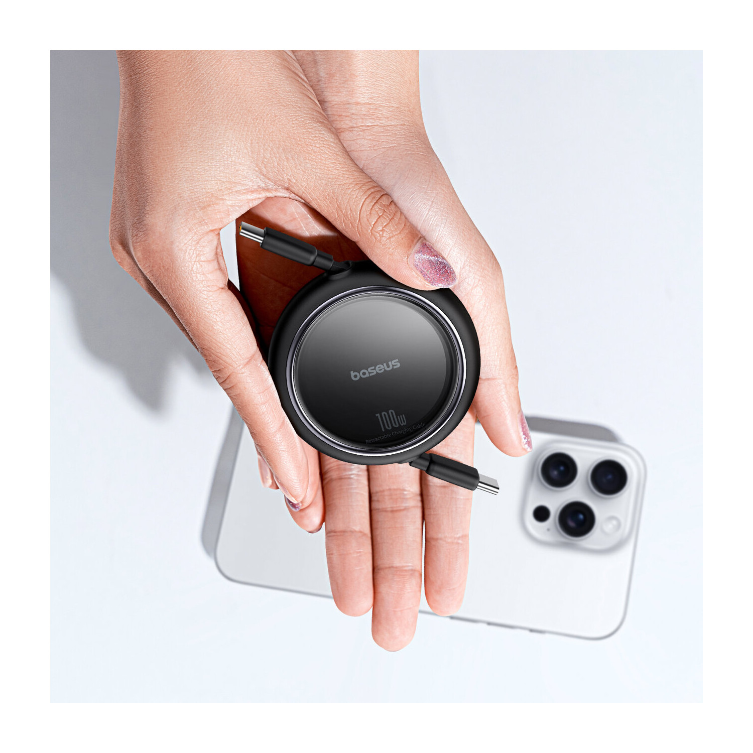 Dłoń osoby trzymająca czarny kabel do ładowania Baseus 100W i biały iPhone.