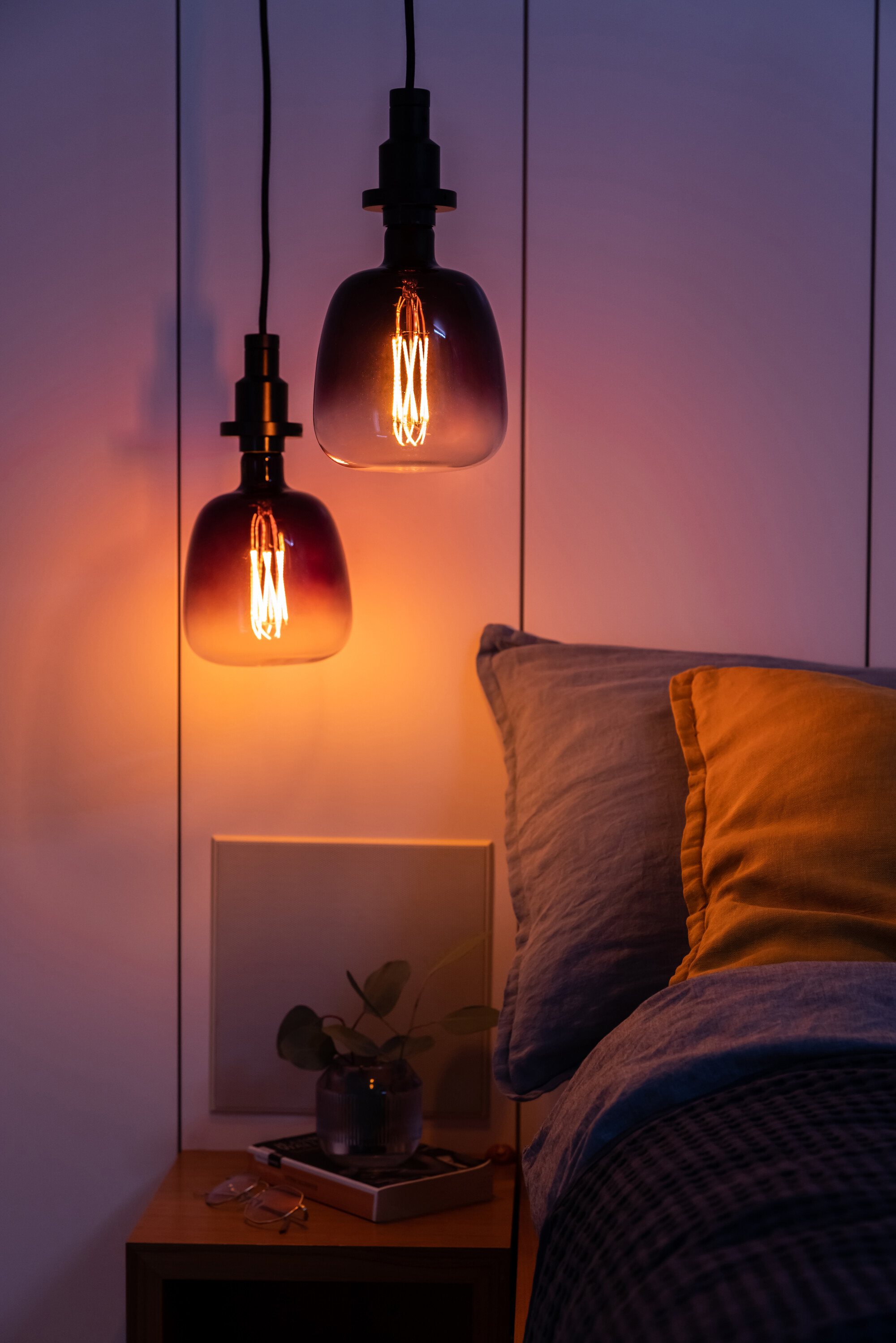 Zwei hängende Glühbirnen mit Bett und Nachttisch im Hintergrund.