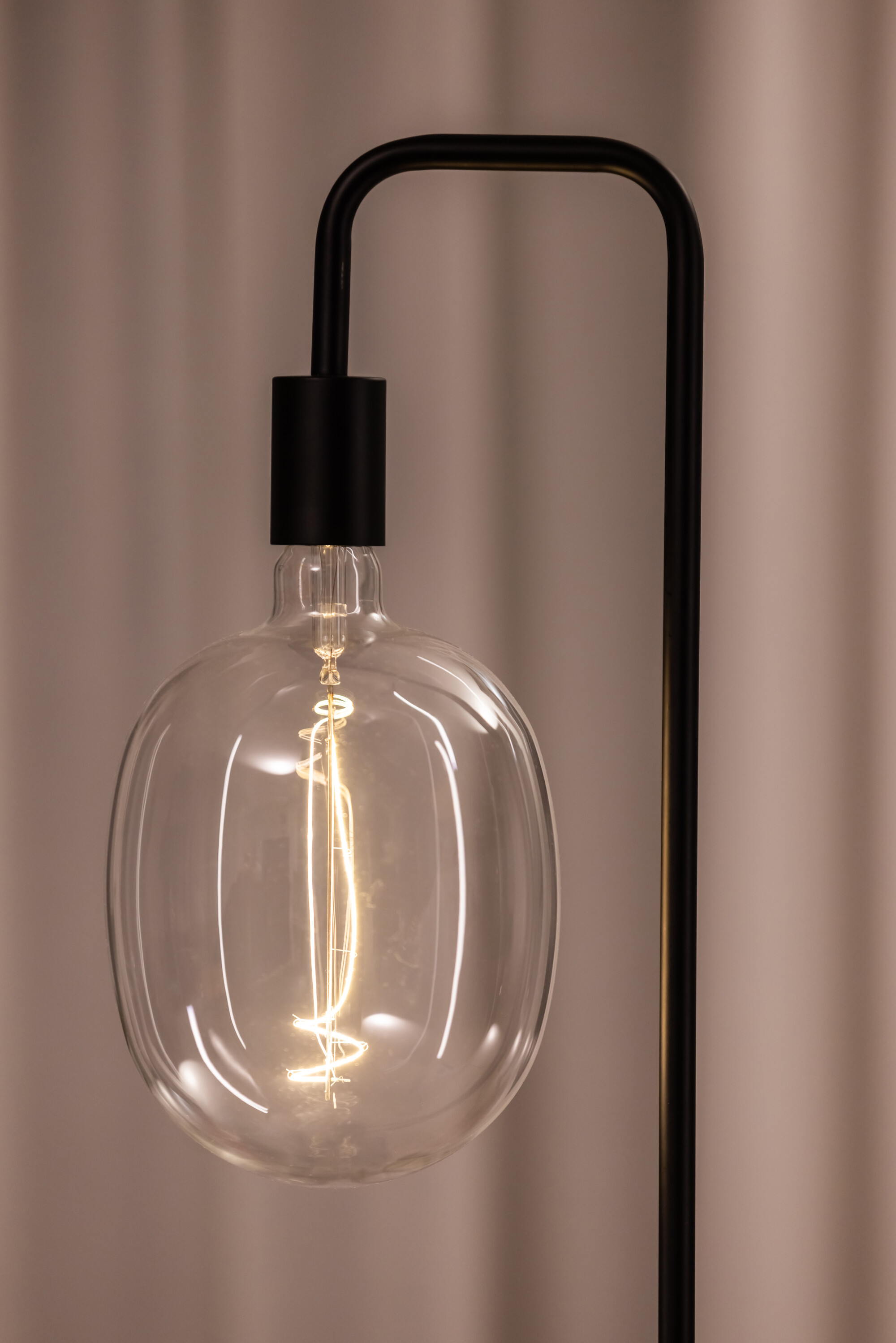 Une lampe noire avec une grosse ampoule transparente. L'ampoule a un filament incandescent.