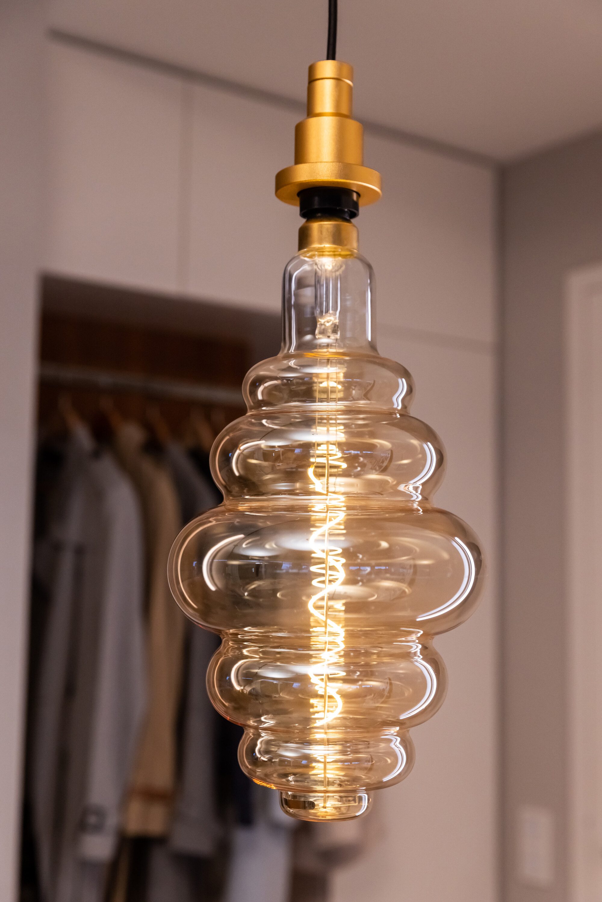Una lampadina decorativa in vetro con la parte superiore dorata, appesa su uno sfondo sfocato di un armadio.