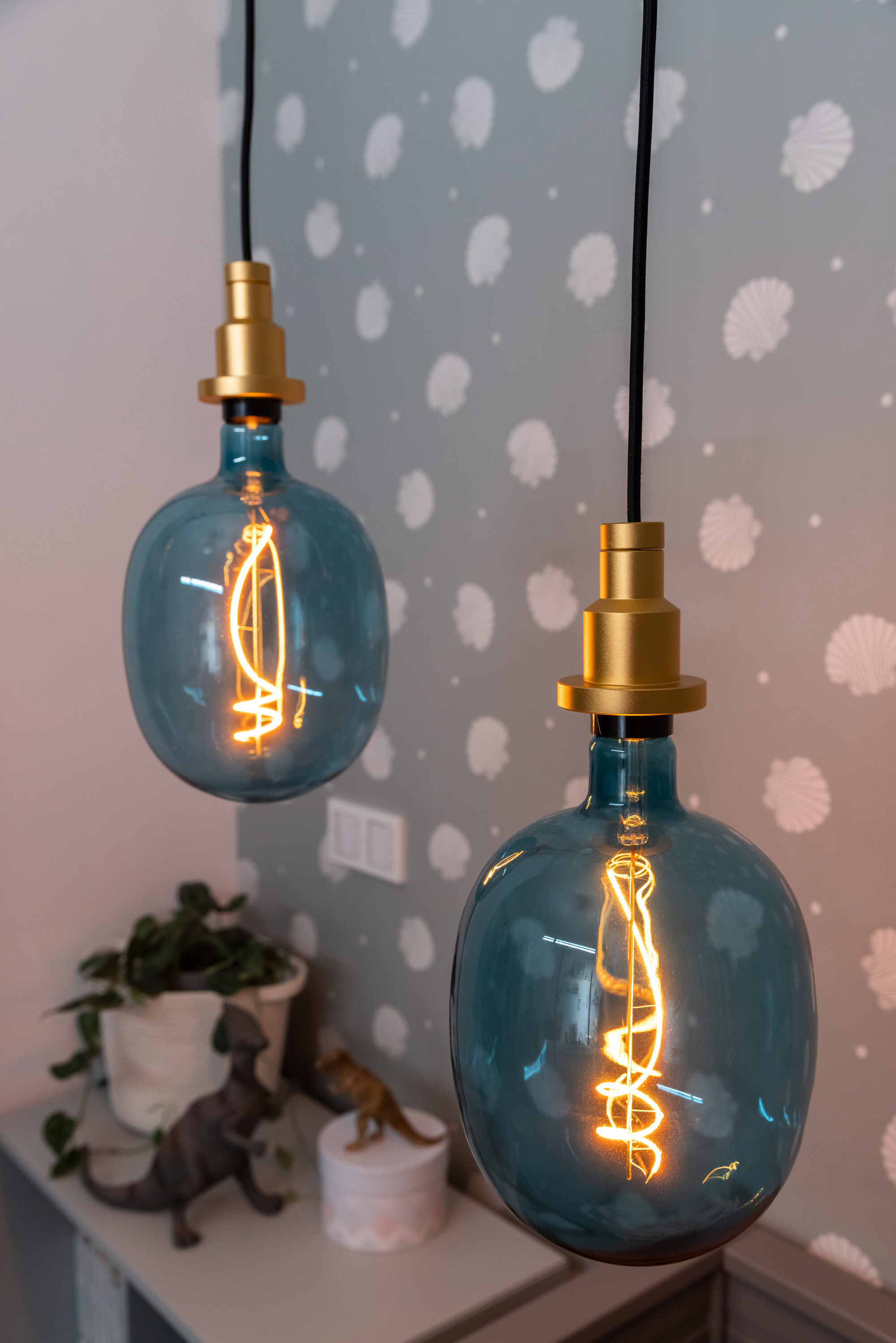 Deux ampoules en verre bleu suspendues au plafond. Un mur rose clair et de petits jouets en arrière-plan.