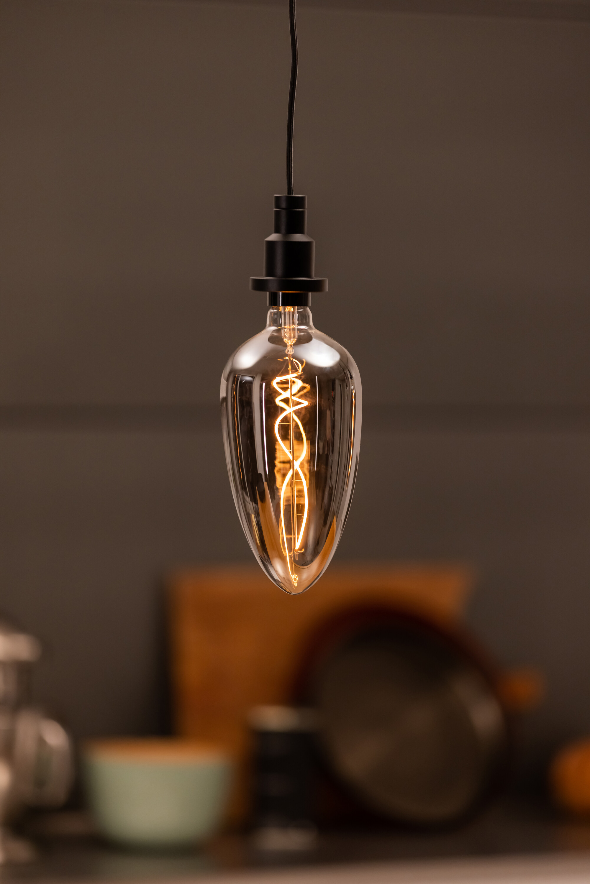Ampoule suspendue avec filament courbé, fixations noires et une lueur chaude, jaune.