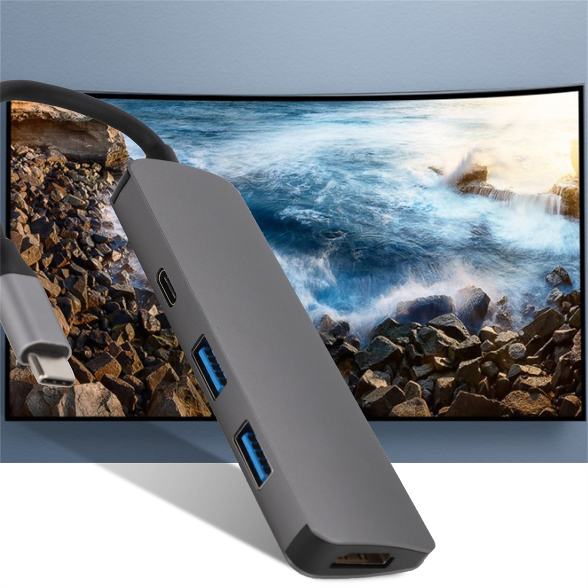 Grauer USB-Hub mit USB-Anschlüssen und USB-C-Anschluss. Ein Monitor zeigt eine felsige Strandszene.