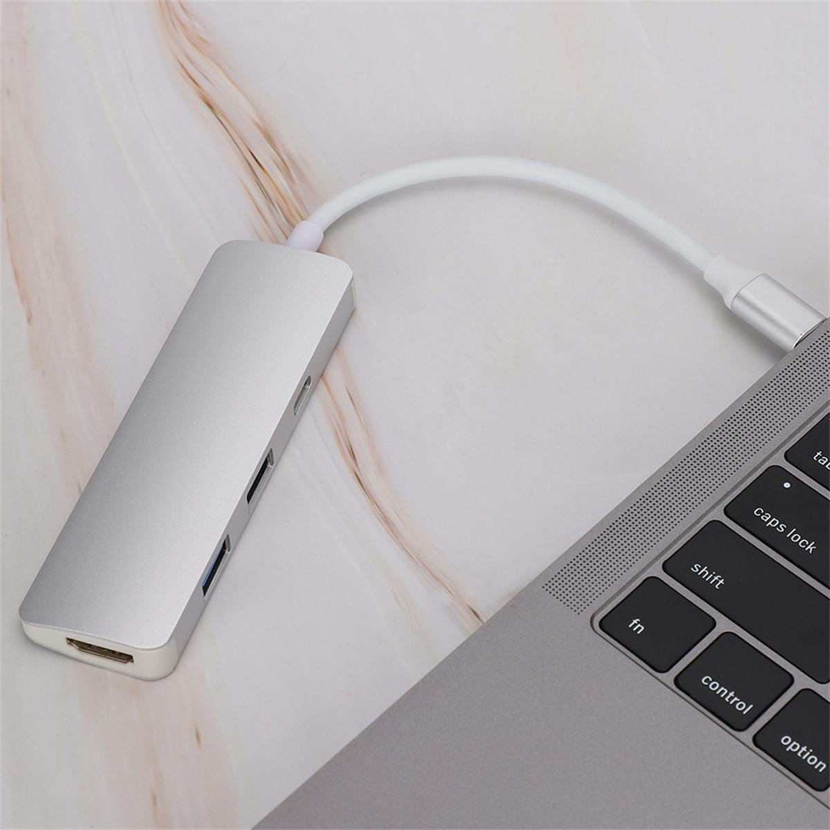 Ein silberner USB-Hub, der mit einem Laptop verbunden ist. HDMI- und USB-Anschlüsse sind sichtbar.