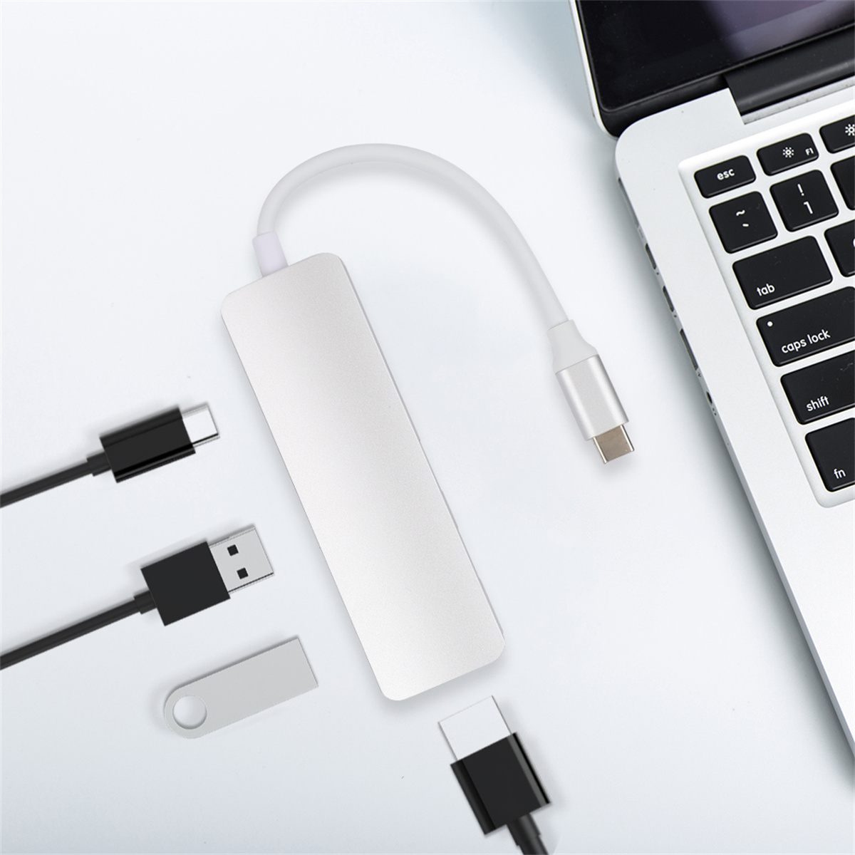 Silberner USB-Hub mit mehreren Anschlüssen und angeschlossenen Kabeln, in der Nähe eines Laptops auf weißem Untergrund.