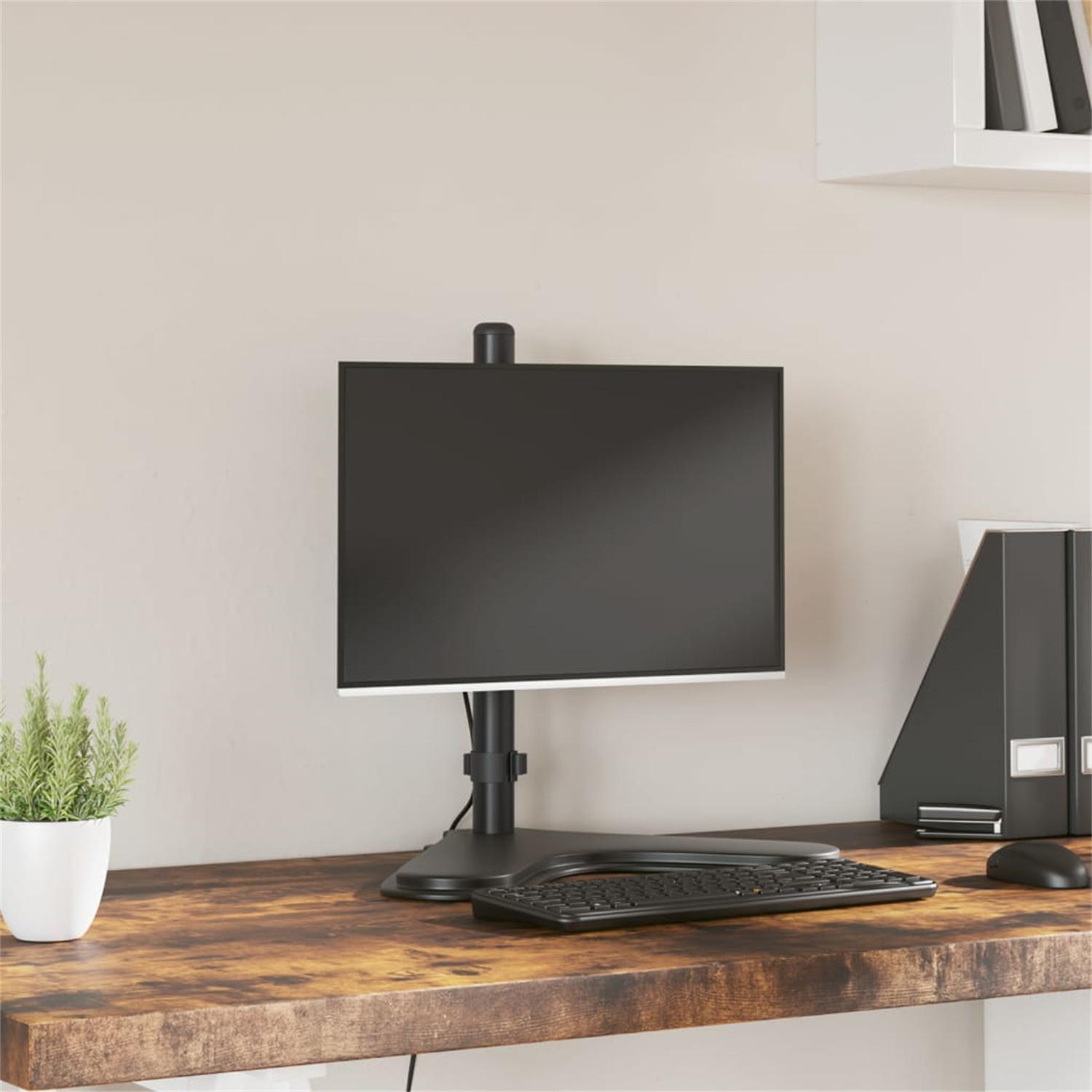 Ein Computermonitor auf einem Schreibtisch montiert, mit schwarzem Bildschirm. Eine Pflanze und eine Tastatur sind daneben.