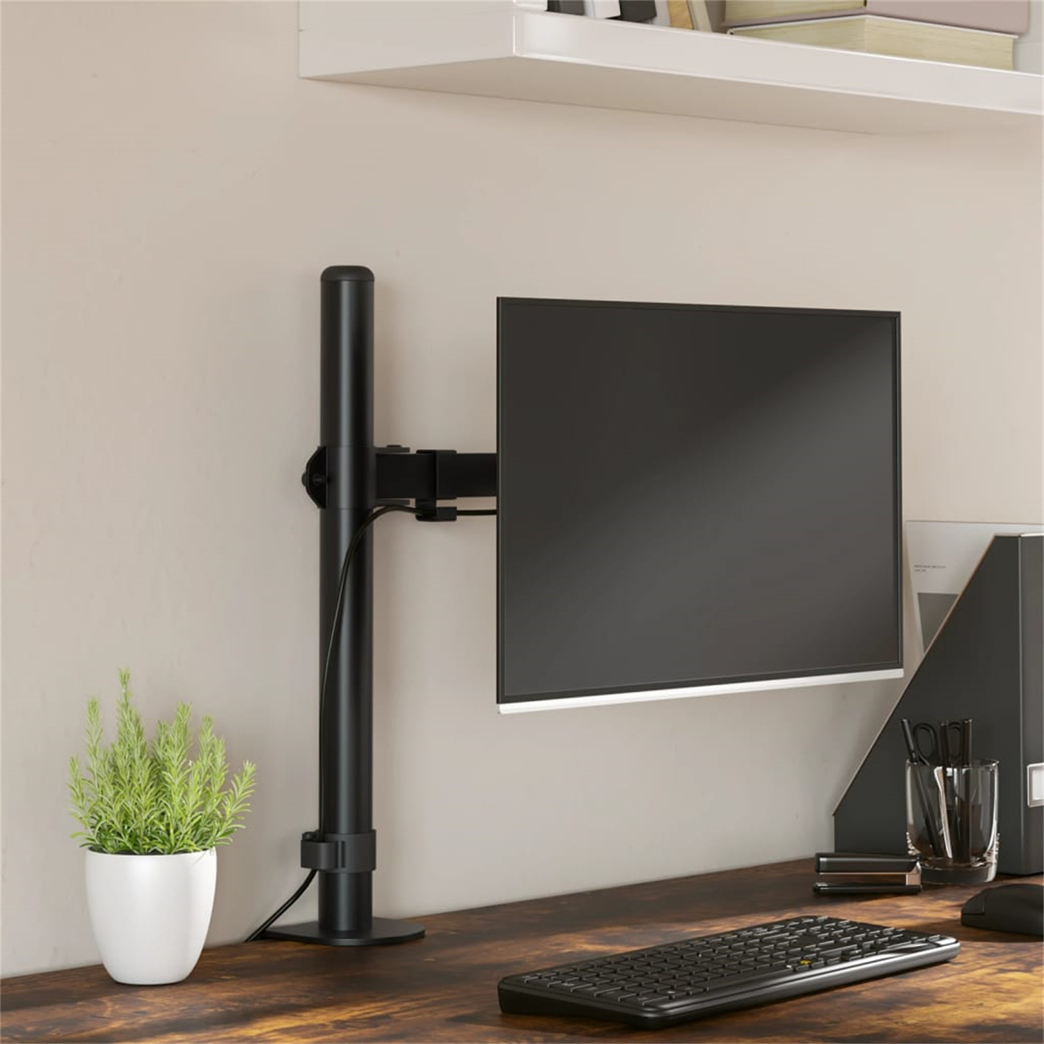 Ein Monitor auf einem schwarzen Ständer montiert. Links ist eine Pflanze, Tastatur und andere Schreibtischartikel.