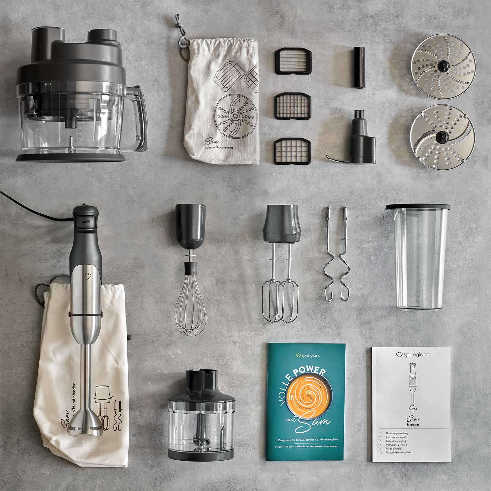 Küchengeräte-Set mit Mixer, Aufsätzen und Zubehör auf grauer Oberfläche. Enthält eine Bedienungsanleitung.