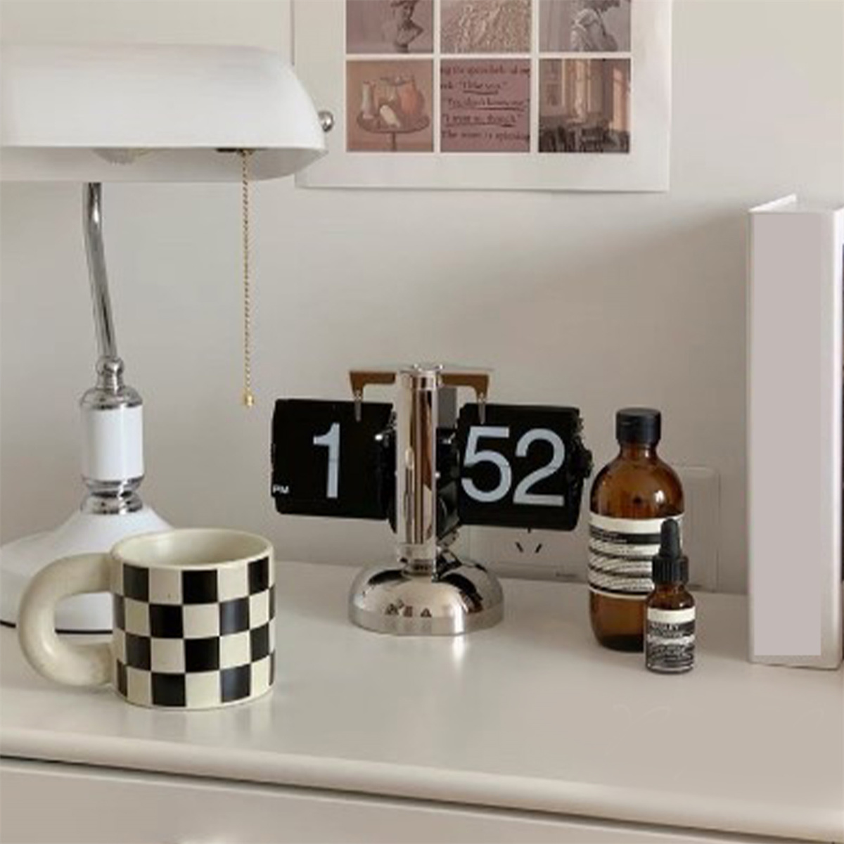 Ein Schachbrettbecher, eine Uhr und eine braune Flasche auf einer weißen Oberfläche, mit einer Lampe.