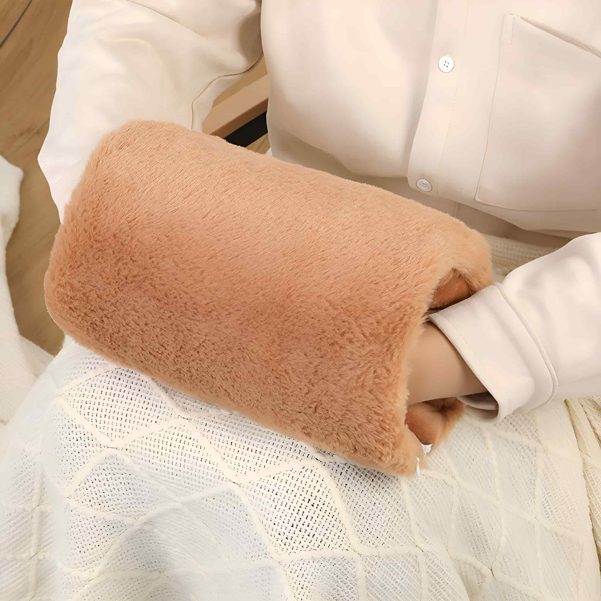 Die Hand einer Person in einem beigefarbenen, flauschigen Handwärmer, sitzend, auf weißem Grund.