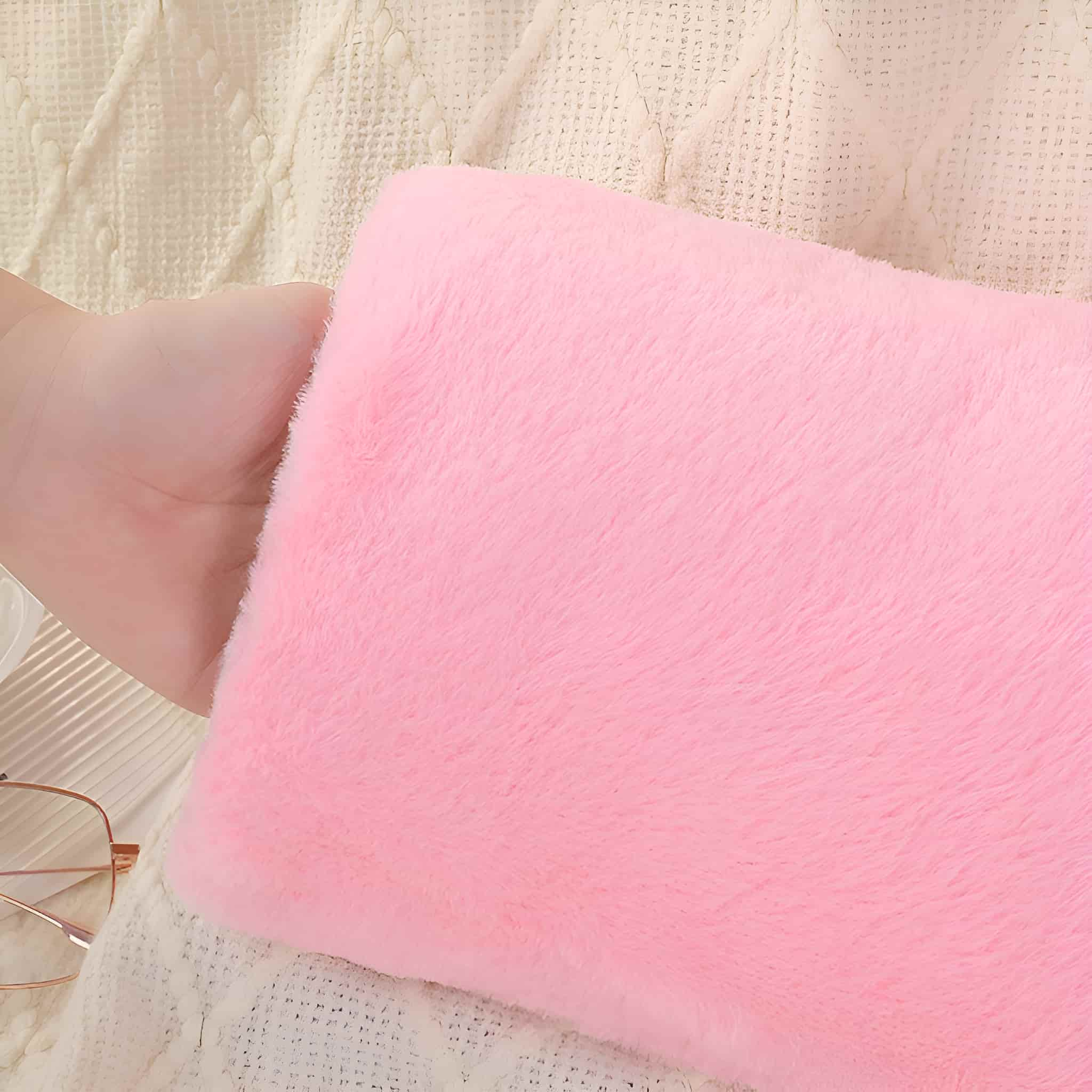 Rosa flauschiges Kissen, auf weißer Strickdecke, auf beiger Oberfläche.