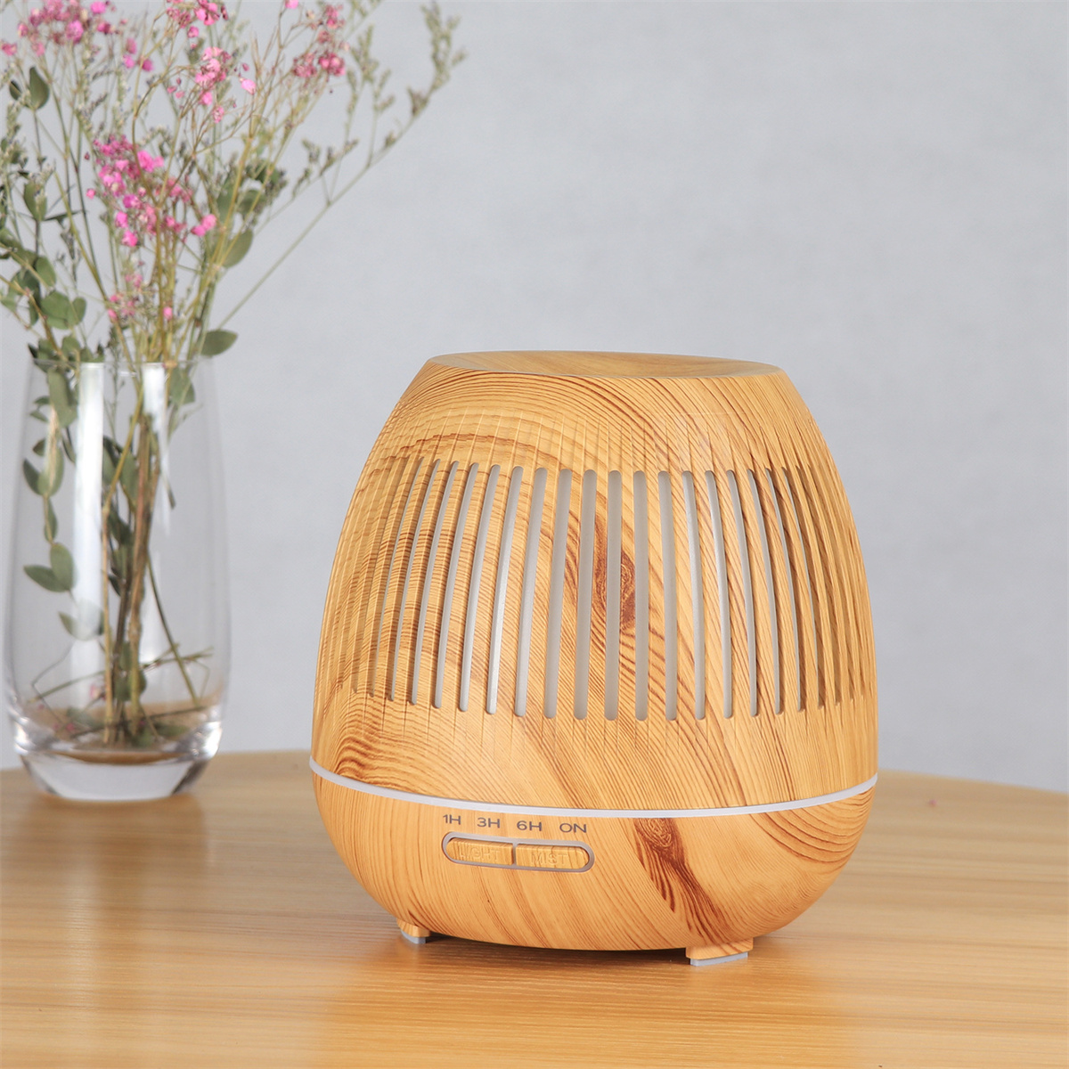 Aroma-Diffusor aus Holz auf einem Holztisch. Vase mit rosa Blumen. Hellgrauer Hintergrund.