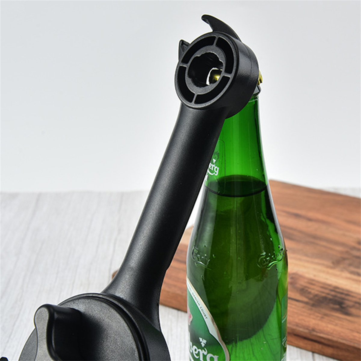 Schwarzer Flaschenöffner öffnet eine grüne Bierflasche. Der Öffner befindet sich auf einem Holzschneidebrett.
