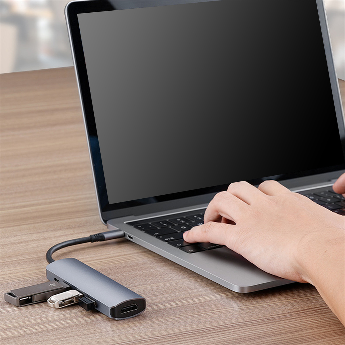 Ein Laptop mit angeschlossenem USB-Hub und eine Hand, die die Tastatur benutzt. Andere USB-Geräte sind ebenfalls sichtbar.
