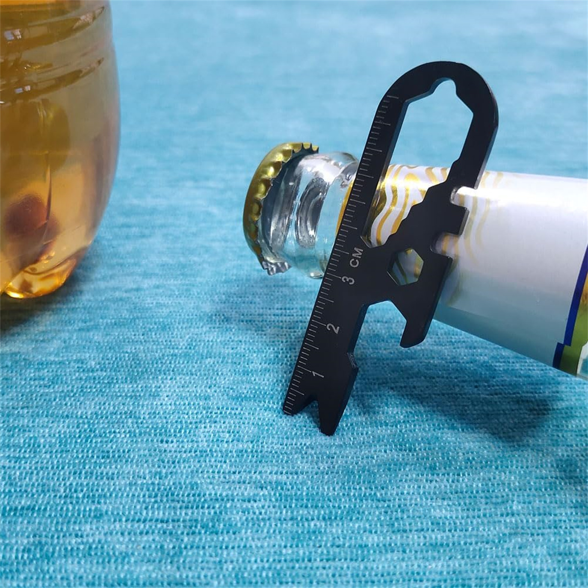 Ein schwarzes Multitool wird in eine Flasche gesteckt, mit einem Lineal und Werkzeugen auf einer blauen Oberfläche.